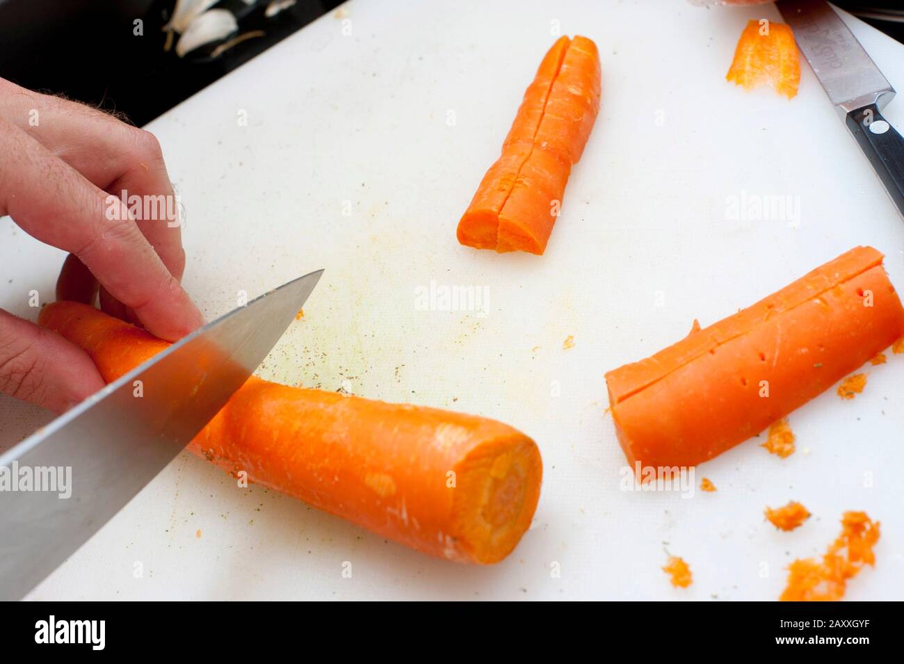 L'uomo che taglia carote intere fresche che ha raschiato e pulito usando un  coltello grande chef mentre prepara le verdure per un pasto Foto stock -  Alamy