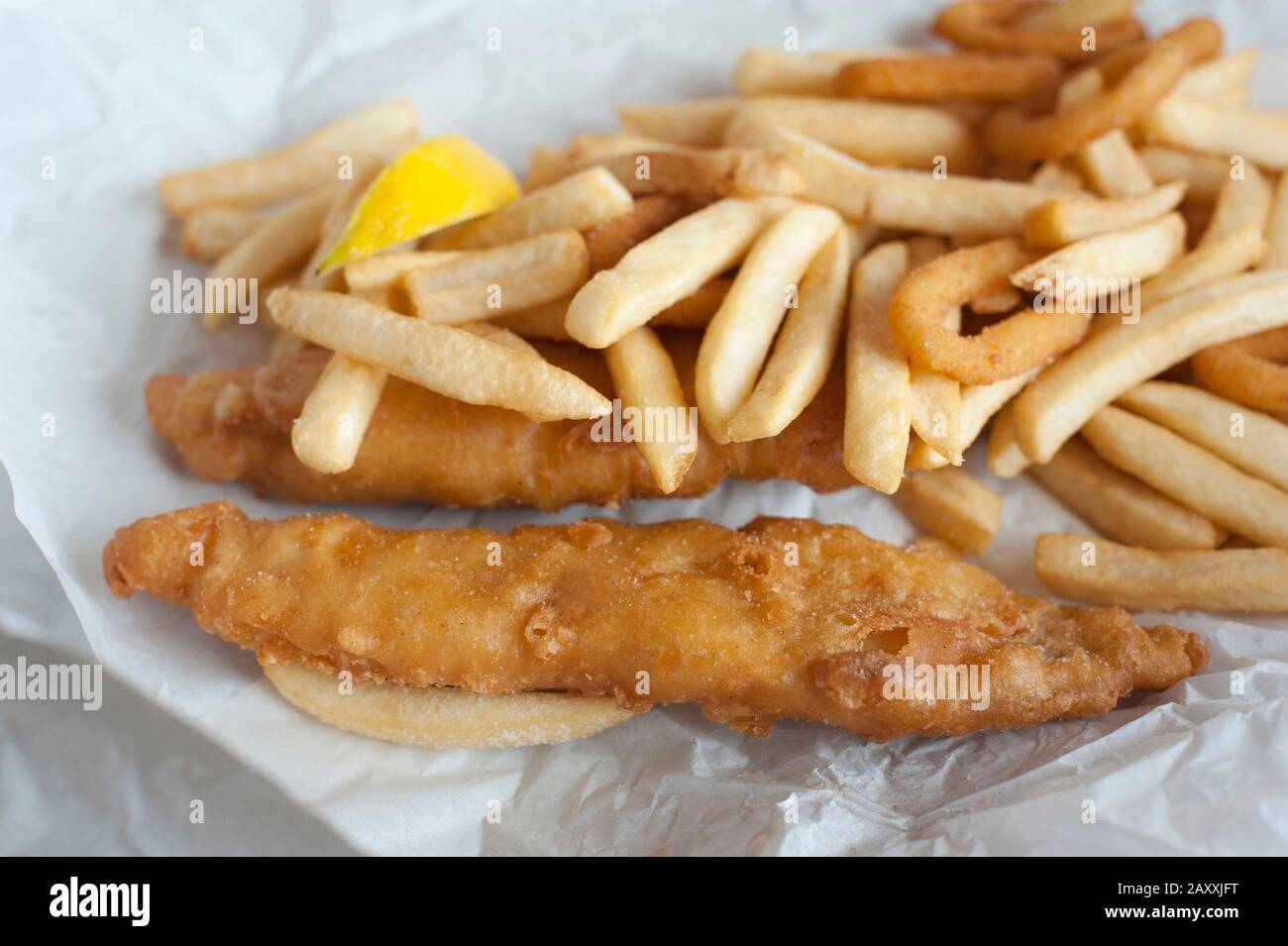 Piatto di takeaway di pesce fritto e patatine fritte su un foglio di carta graseproof sbriciolato Foto Stock