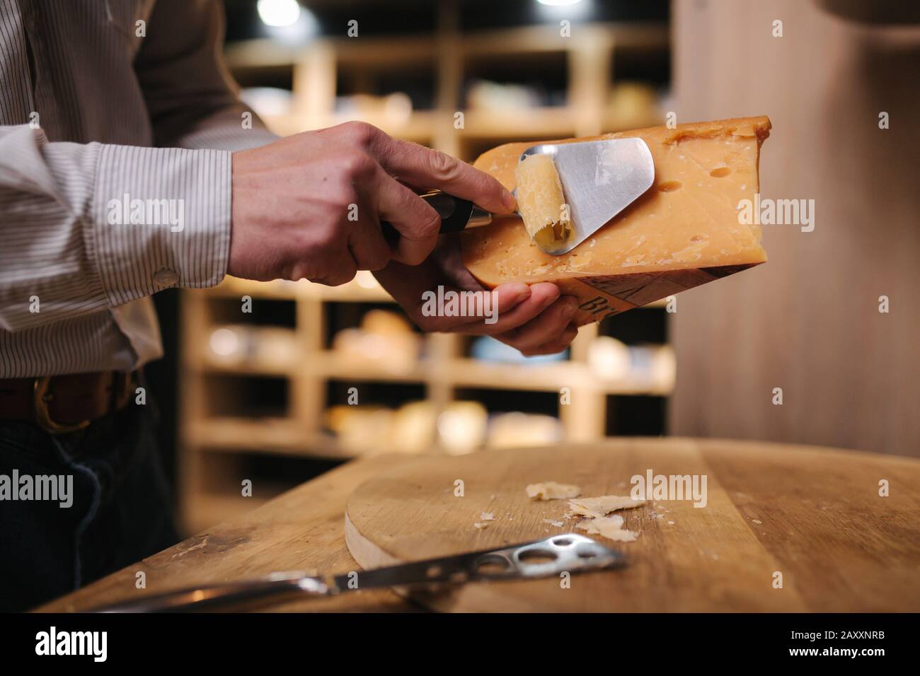 Uomo affettare un pezzetto di formaggio per il gusto. Giovane lavoratore utilizzare coltello speciale per il formaggio Foto Stock