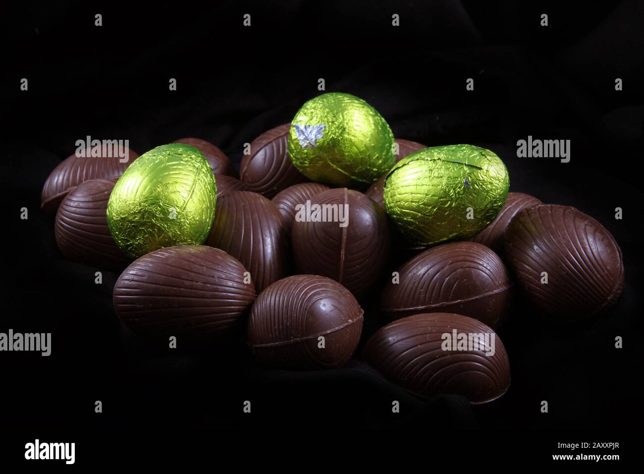Pila di calce di colore verde o giallo stagnola avvolto e confezionato le uova di Pasqua di cioccolata contro uno sfondo nero. Foto Stock