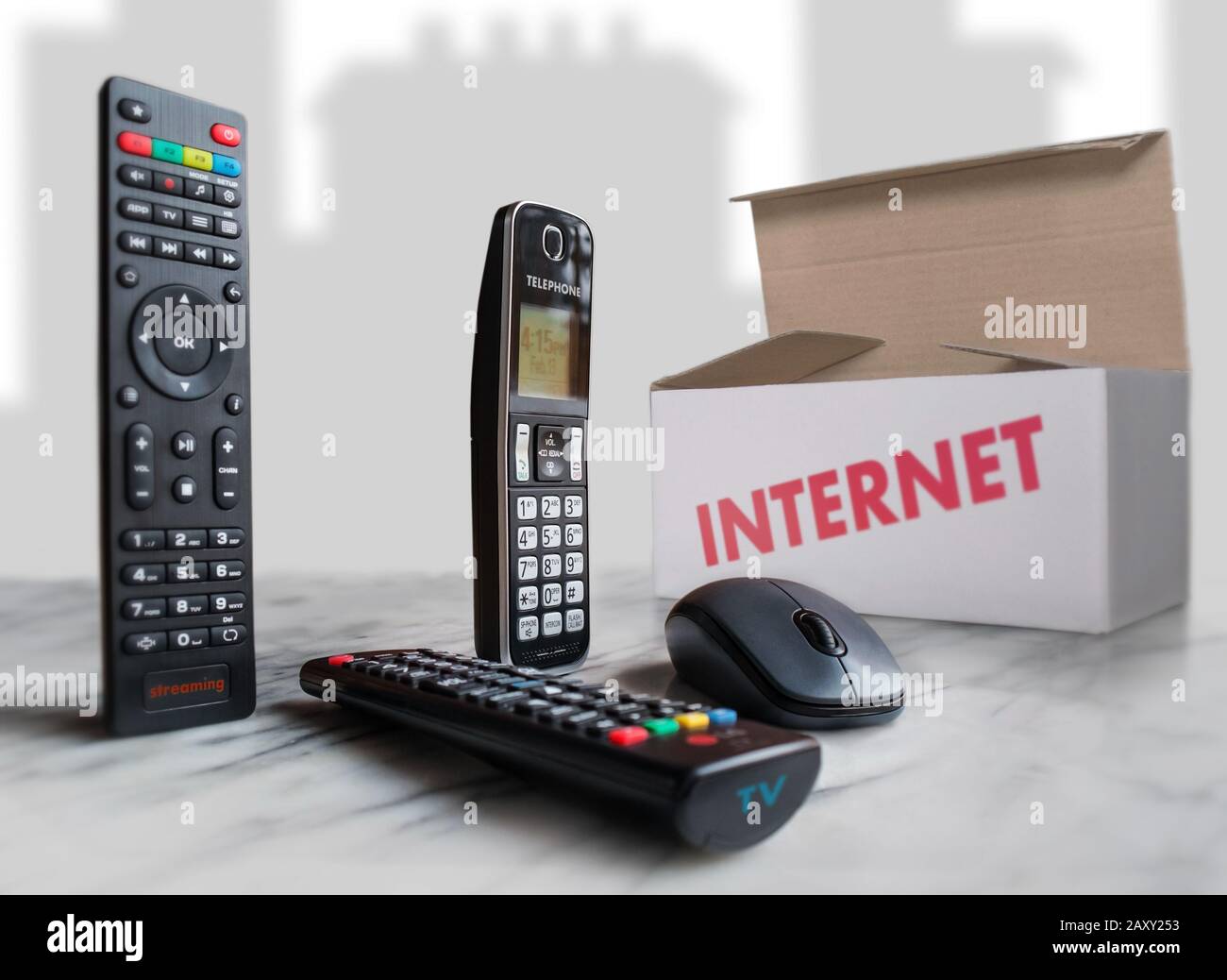 Su una superficie chiara vediamo un telecomando per lo streaming, un altro per TV, un mouse per computer e una scatola che rappresenta il pacchetto di servizi. Foto Stock