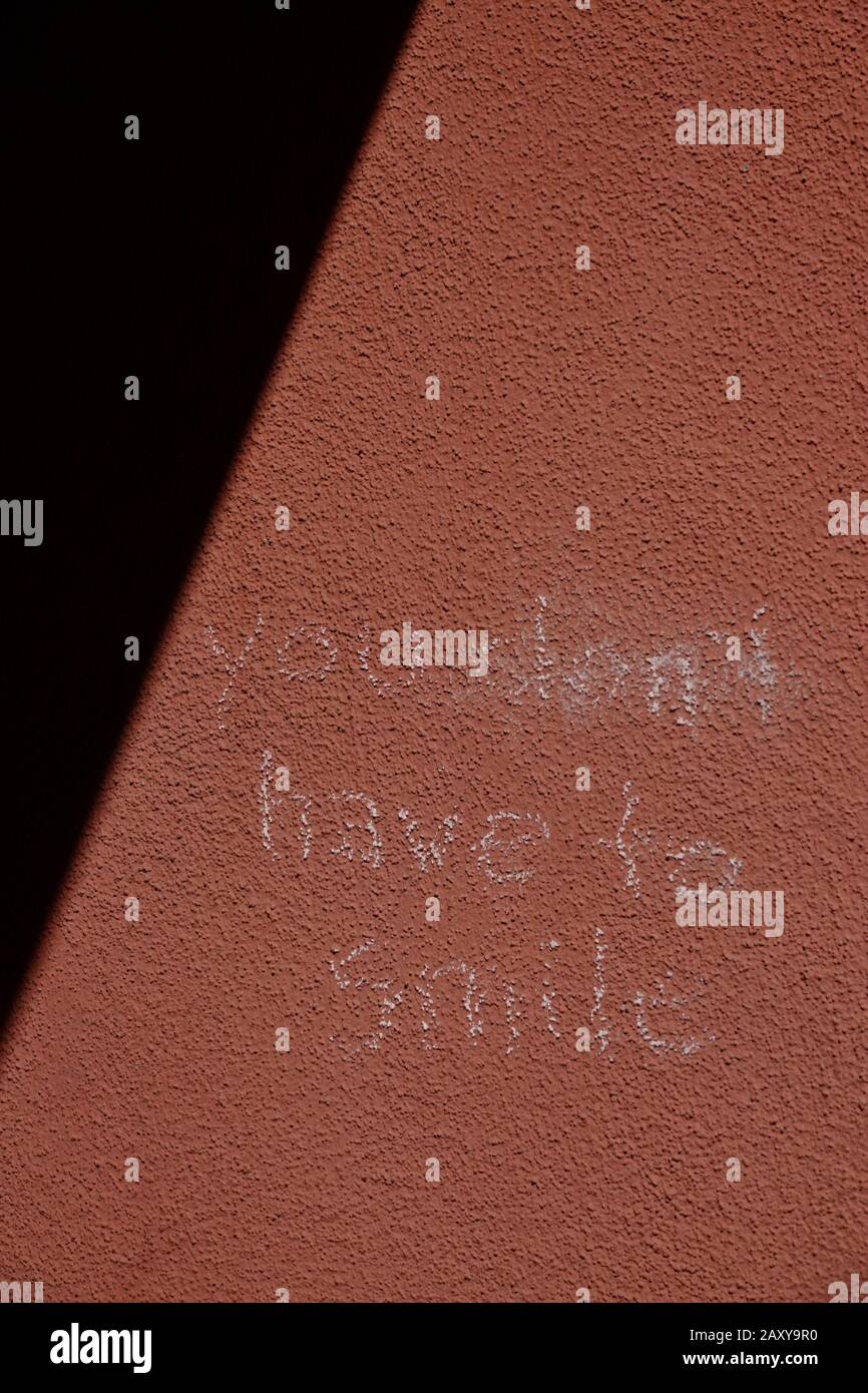 Un messaggio su un muro scritto in gesso dice "non devi sorridere" Foto Stock
