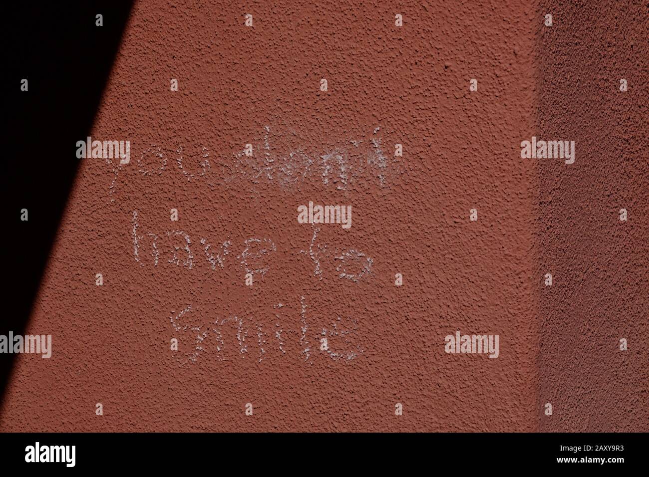 Un messaggio su un muro scritto in gesso dice "non devi sorridere" Foto Stock