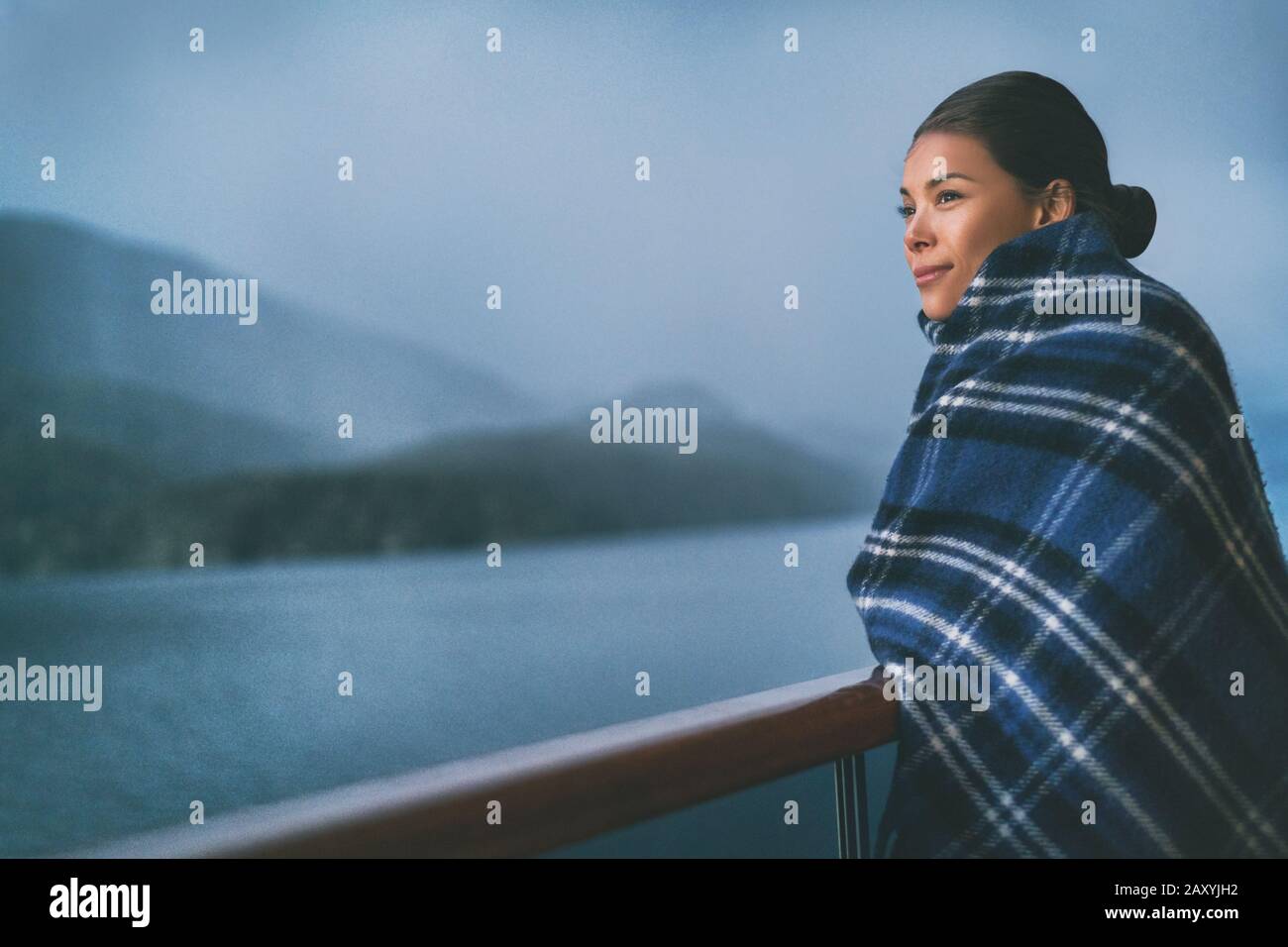 Passeggeri della nave da crociera in vacanza in Alaska, godendosi il paesaggio al tramonto sul ponte suite con balcone e lana tiro in freddo tempo. Donna turistica asiatica rilassante durante le vacanze estive crociera avventura. Foto Stock