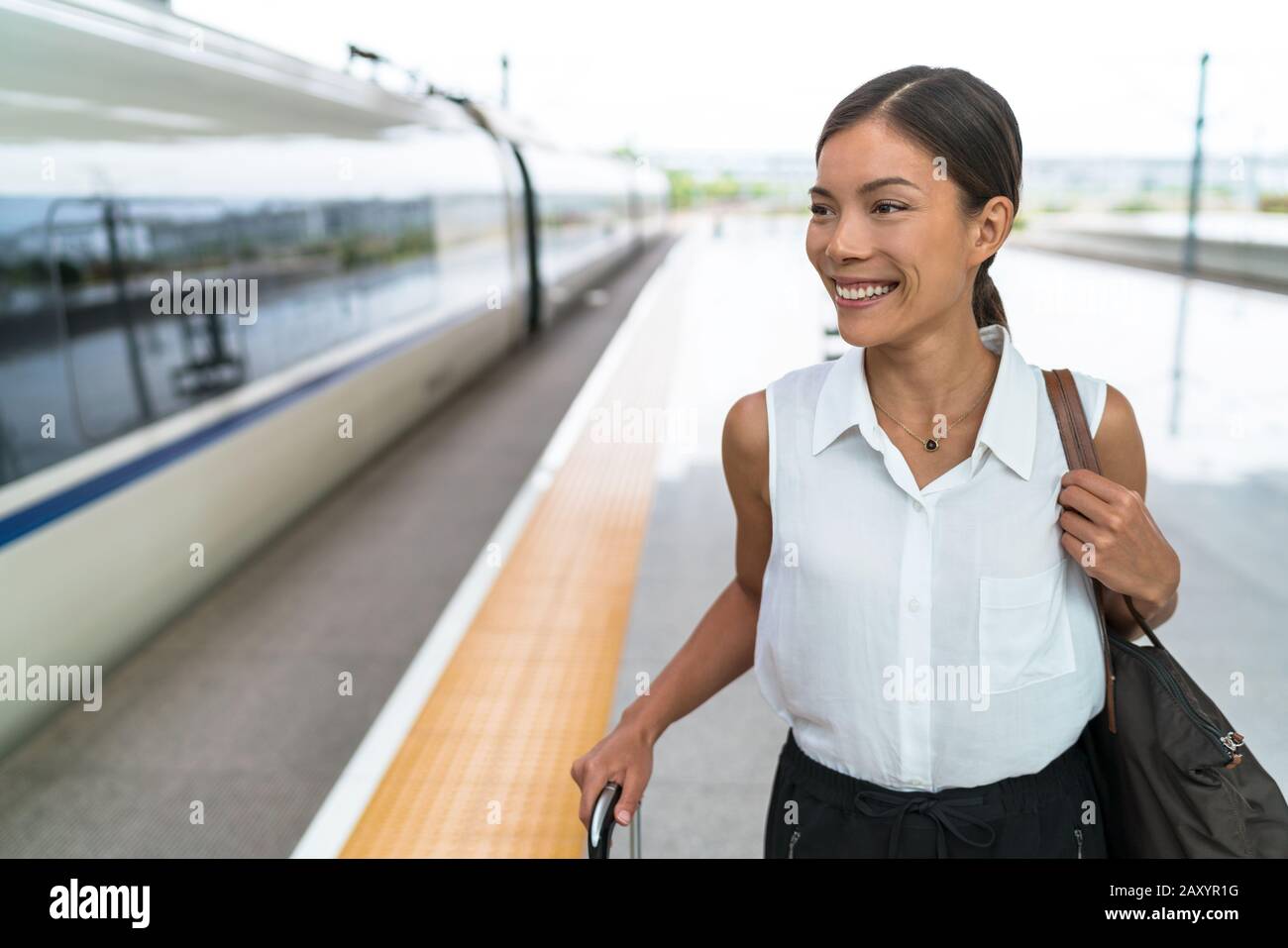 Felice viaggiatore asiatico sorridente andare in treno viaggio in business class. Bella donna con bagaglio a mano che lascia su trasporto di lusso. Businesswoman pendolari a lavorare al mattino. Foto Stock