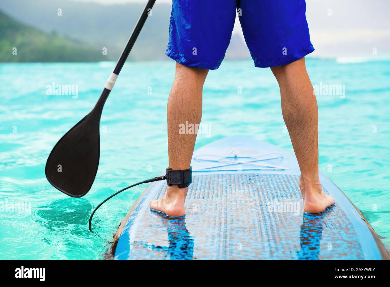 Paddle board uomo che fa stand-up paddleboard sull'oceano. Paddleboarding atleta su SUP surf board su Hawaii Beach Travel. Primo piano delle gambe a bordo. Foto Stock