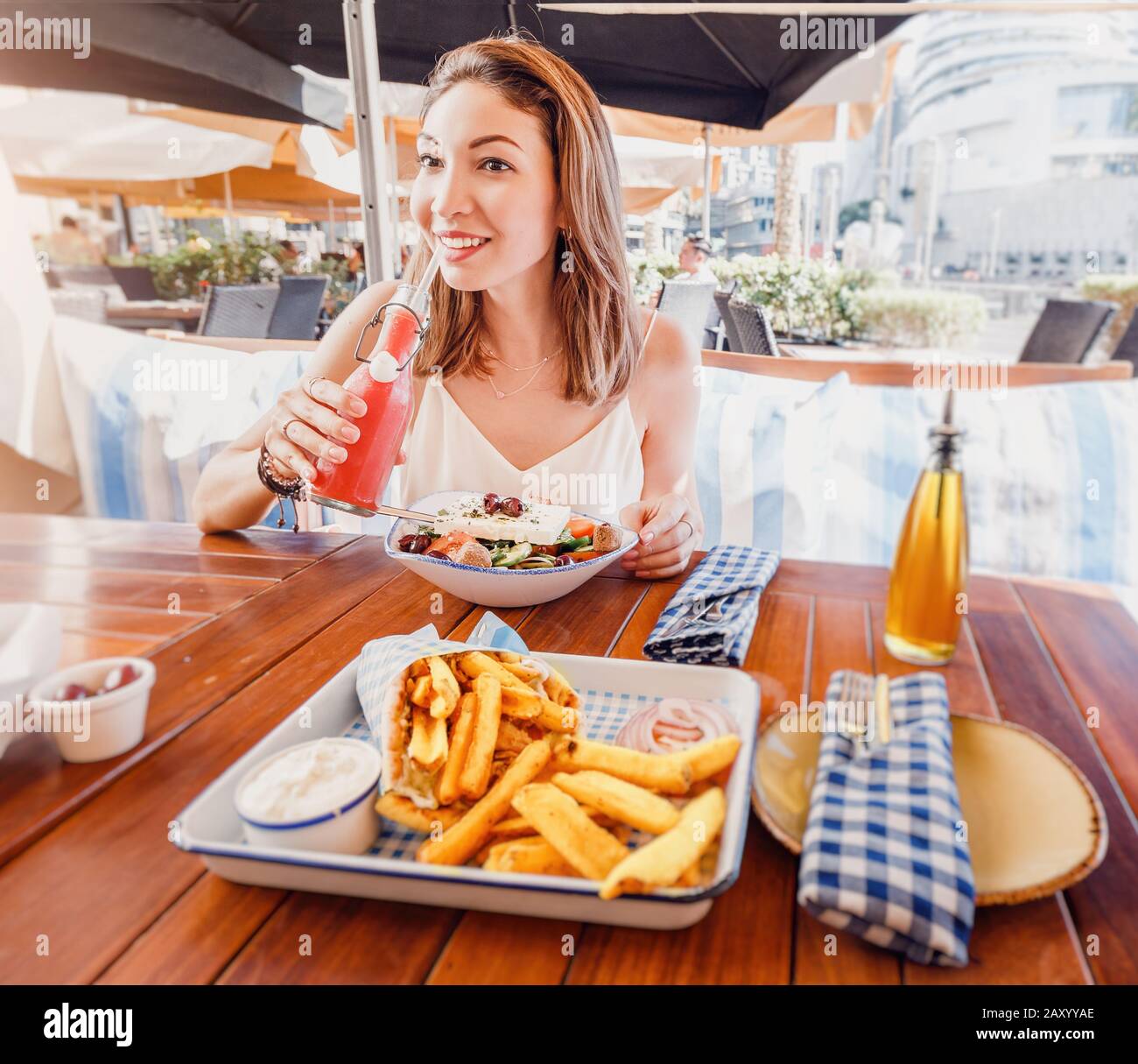 Allegra ragazza turistica prova cucina greca in un ristorante locale. Sul tavolo insalata tradizionale Horiatiki e Gyros a Pita Foto Stock