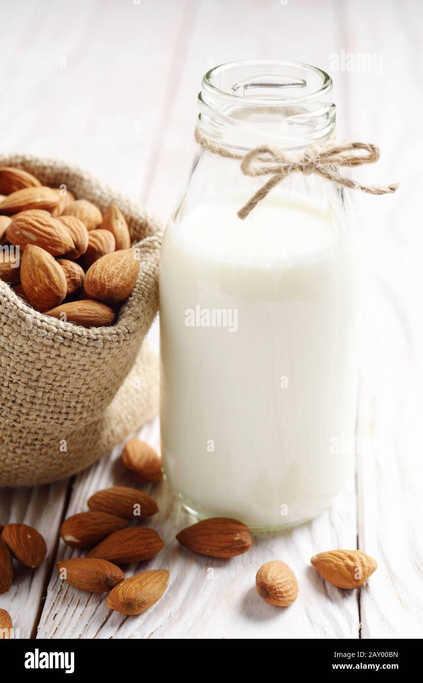 Latte o yogurt in una bottiglia di vetro bianco sul tavolo di legno con le mandorle nel sacco di canapa a parte Foto Stock