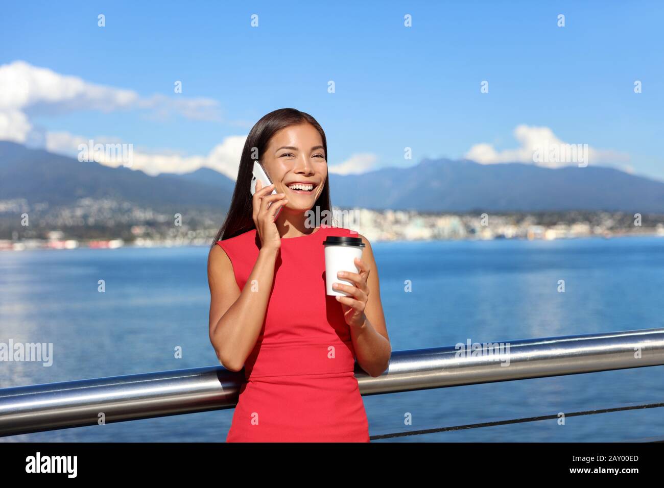 Felice business donna che parla al telefono mentre si beve caffè all'aperto in estate, paesaggio di Vancouver in background. Donna d'affari lavoro stile di vita della città. Foto Stock