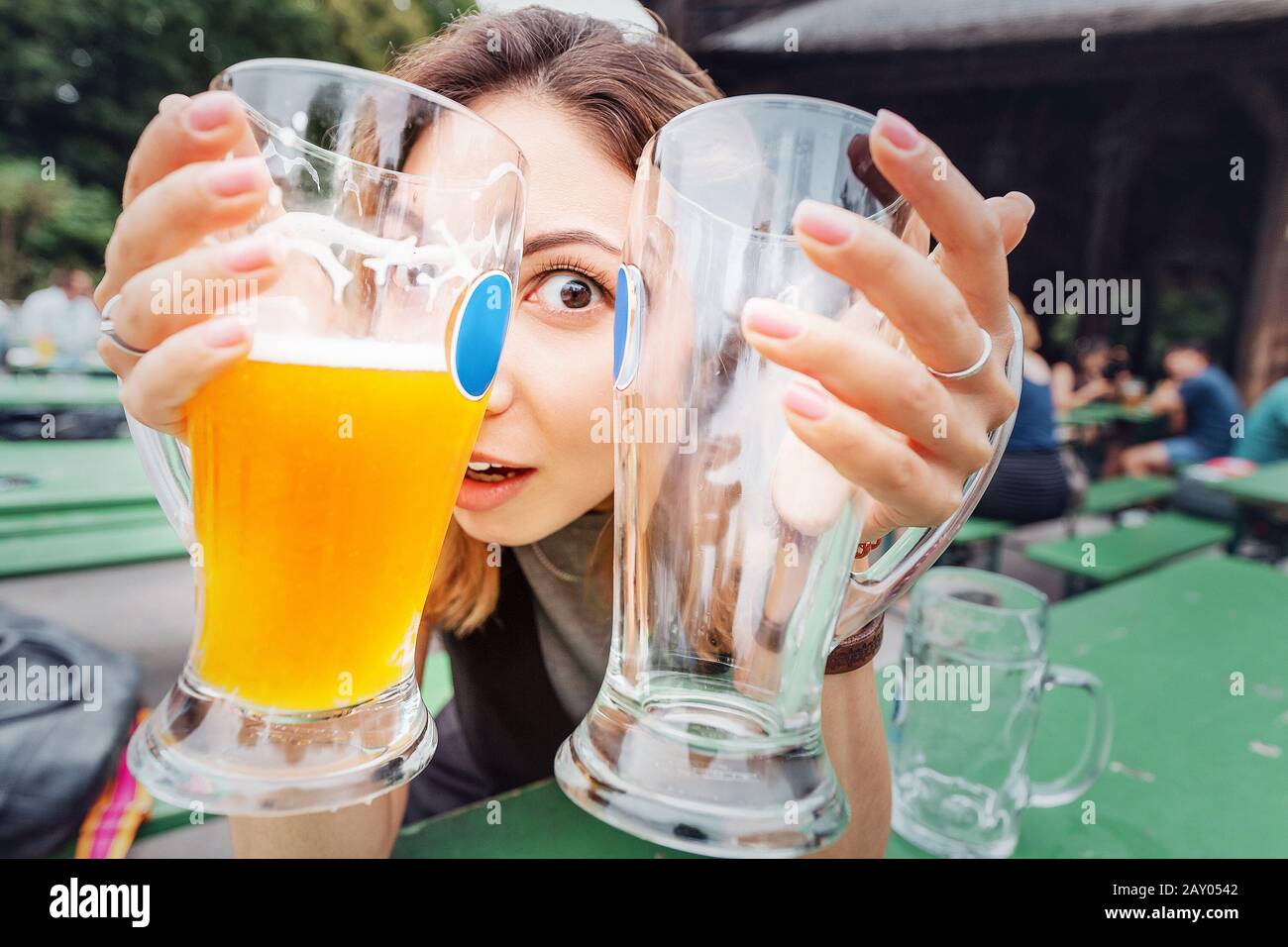 Ragazza asiatica divertente e folle con due Birre sulla terrazza del ristorante birreria in Germania. Il concetto di un hangover e Oktoberfest viaggio Foto Stock