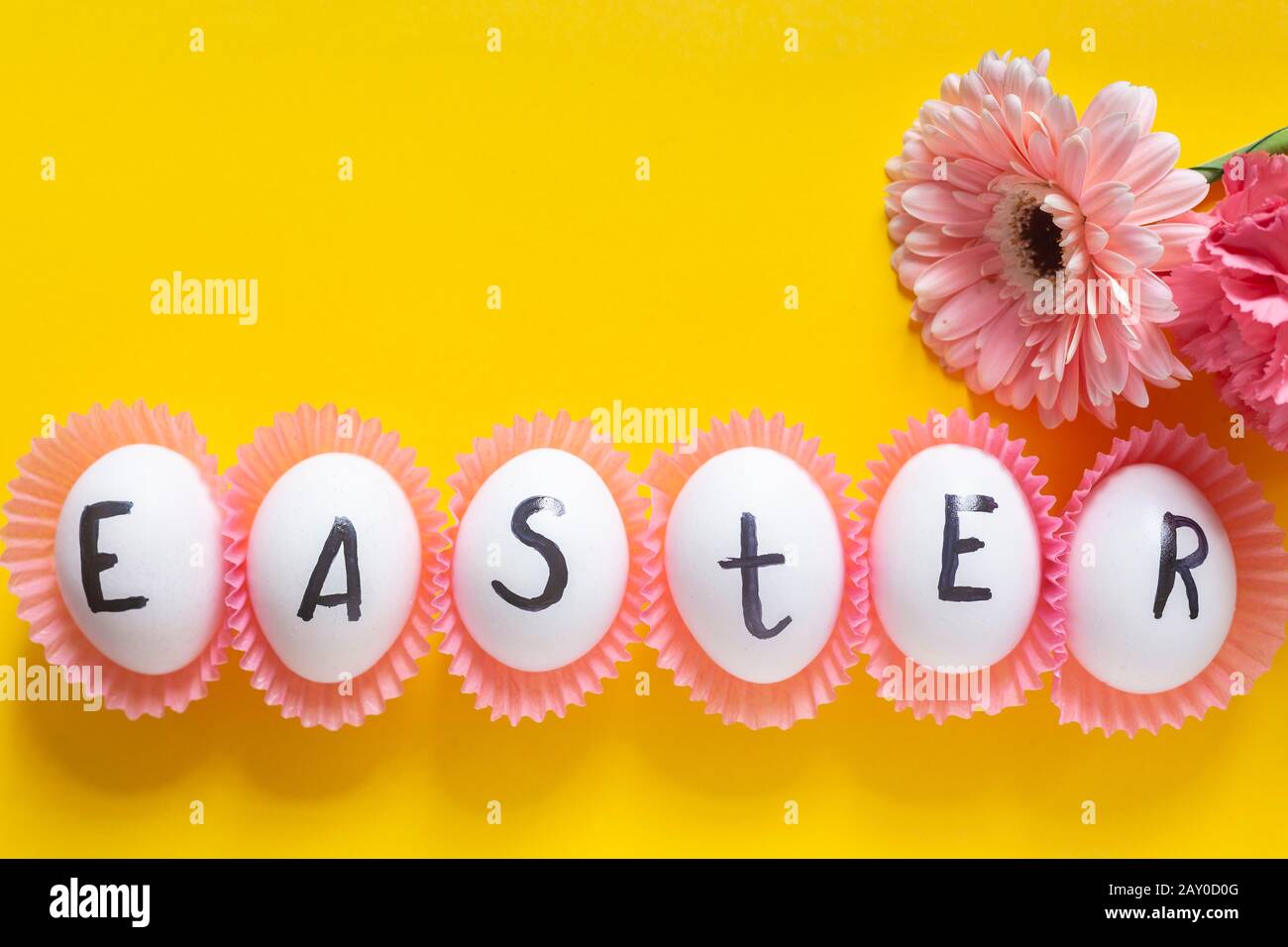 Luminosa immagine di Pasqua con fiori freschi di primavera sullo sfondo giallo. Uova bianche con testo - Pasqua su sfondo luminoso e colorato Foto Stock