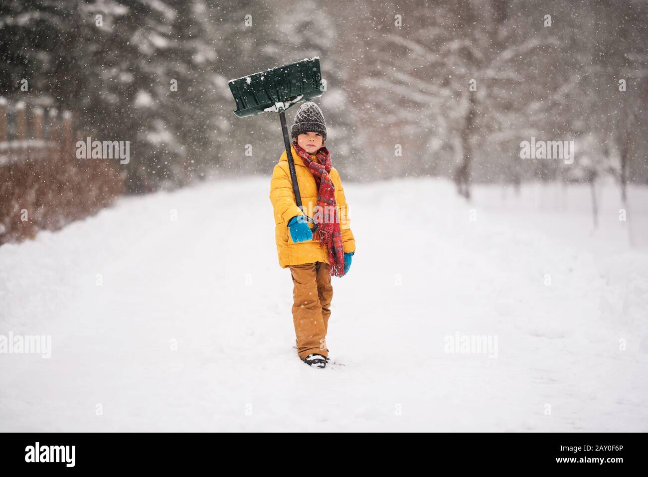 Ragazzo con una pala in piedi nella neve su una lunga strada coperta di neve, Wisconsin, Stati Uniti Foto Stock