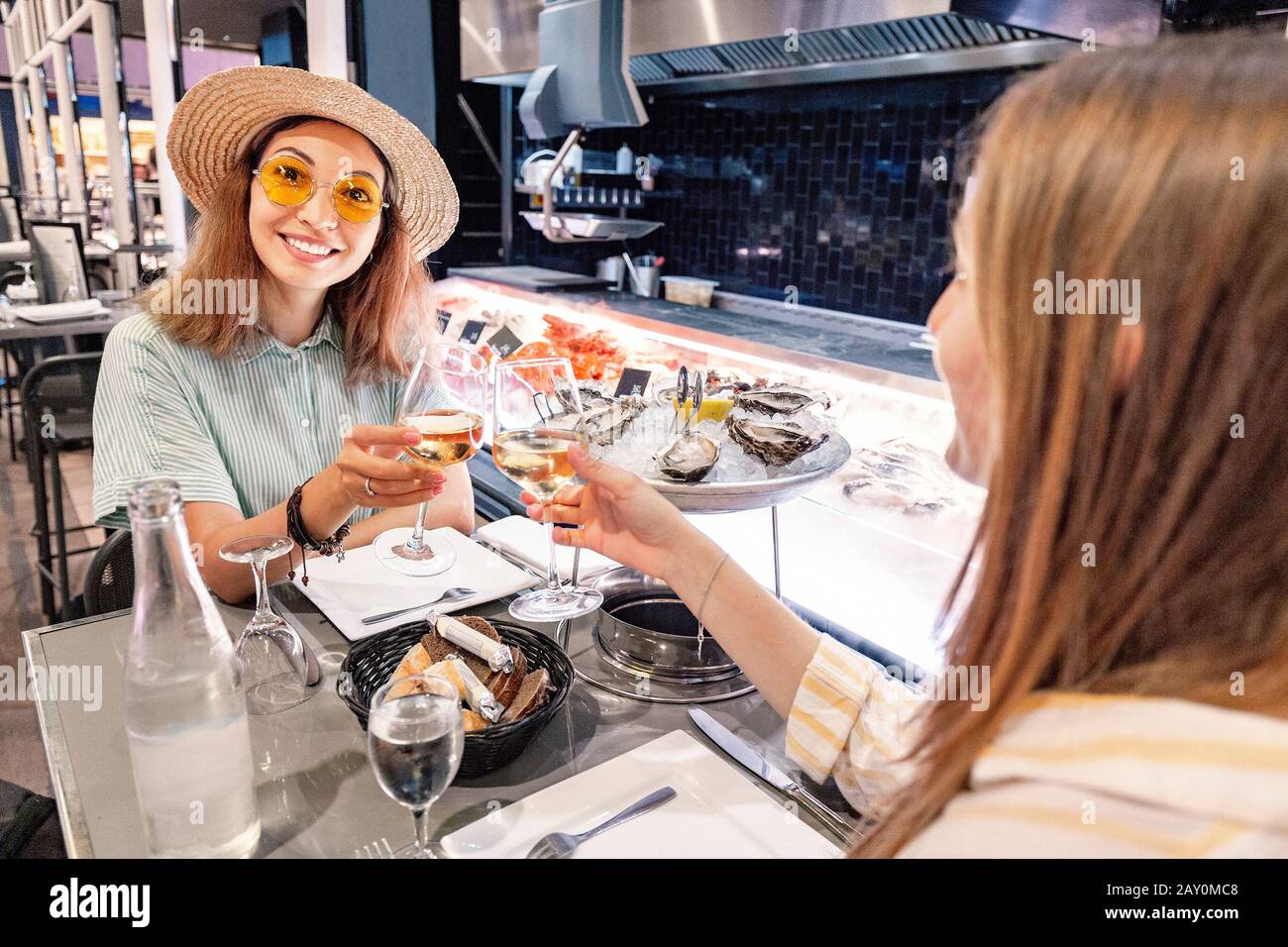 Due amici femminili in un ristorante che mangia ostriche e crostacei e beve vino bianco Foto Stock