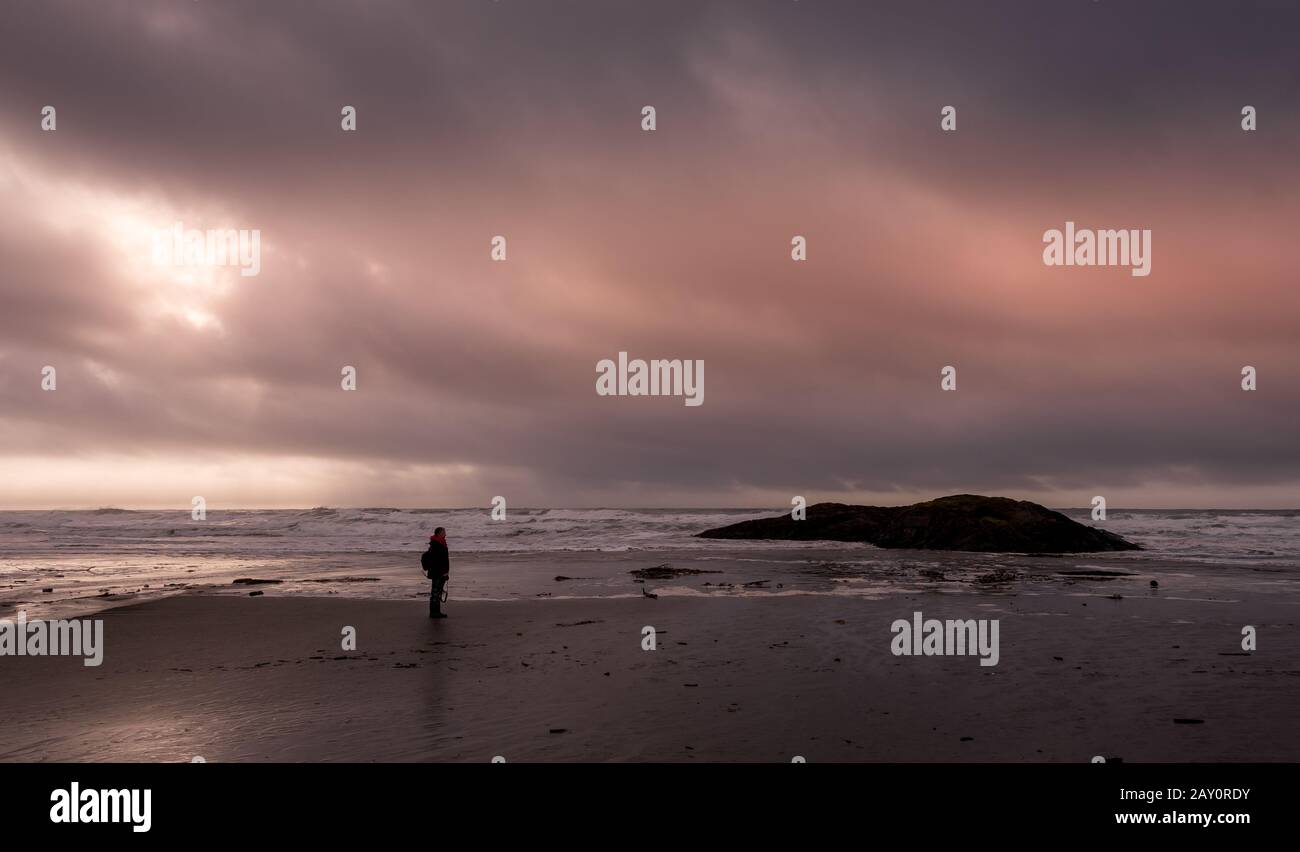 Donna in piedi su una spiaggia al tramonto durante una tempesta, Canada Foto Stock