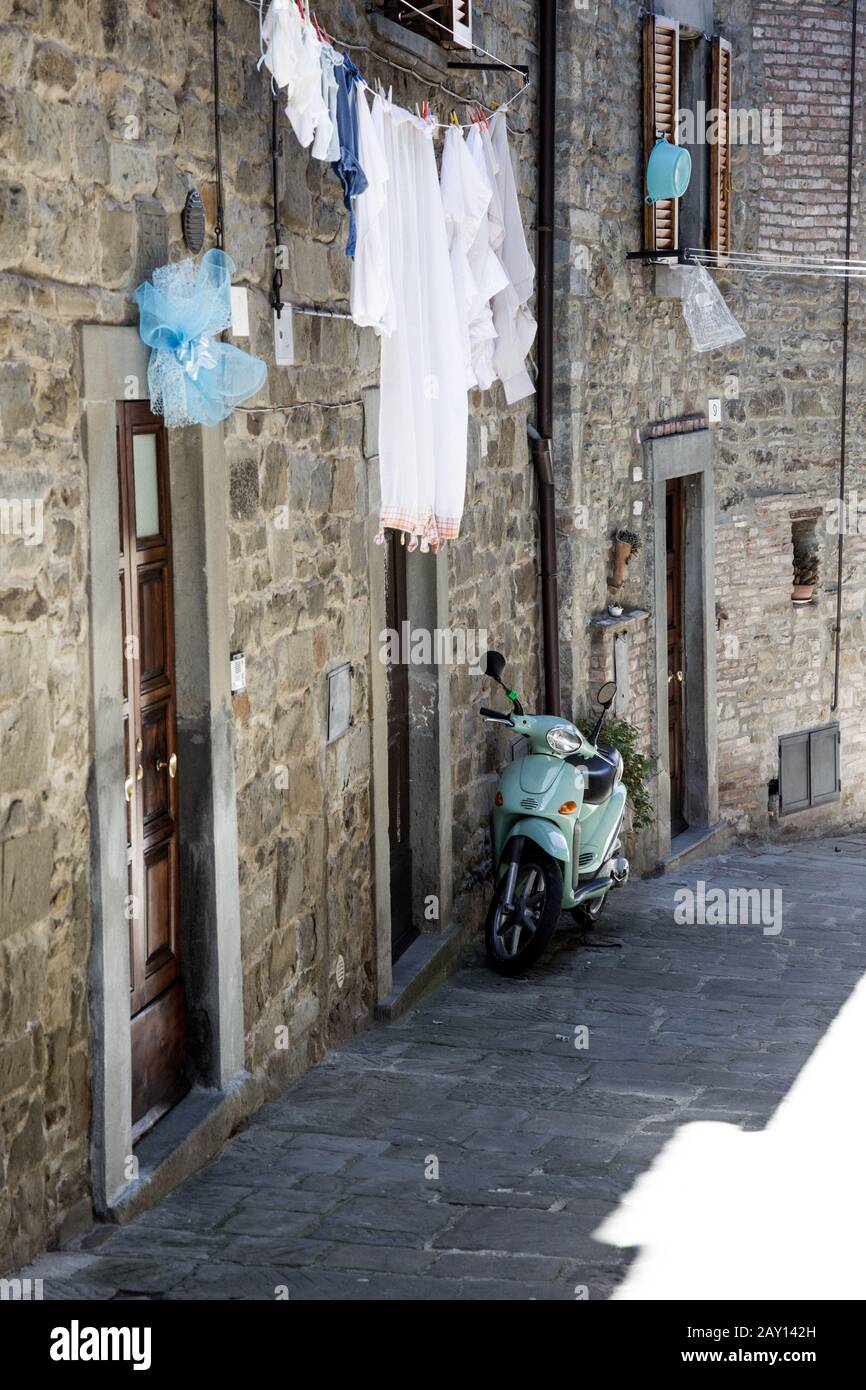 Via Toscana con Vespa / Incantevole stradina della piccola città italiana Cortona con scooter parcheggiato Foto Stock