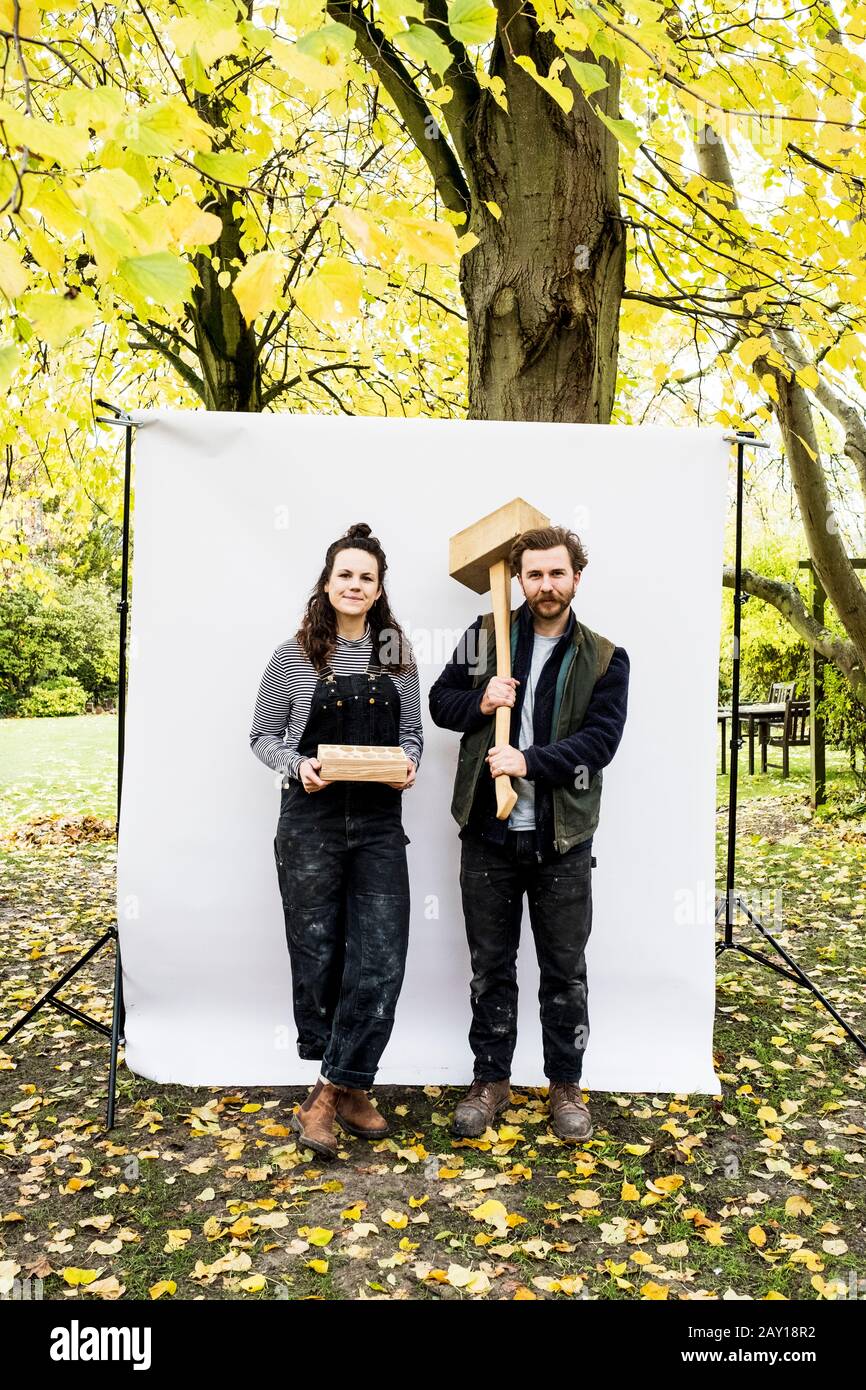 Ritratto di donna e bearded uomo tenendo blocchi di legno in piedi di fronte a sfondo bianco in un giardino, guardando la fotocamera. Foto Stock