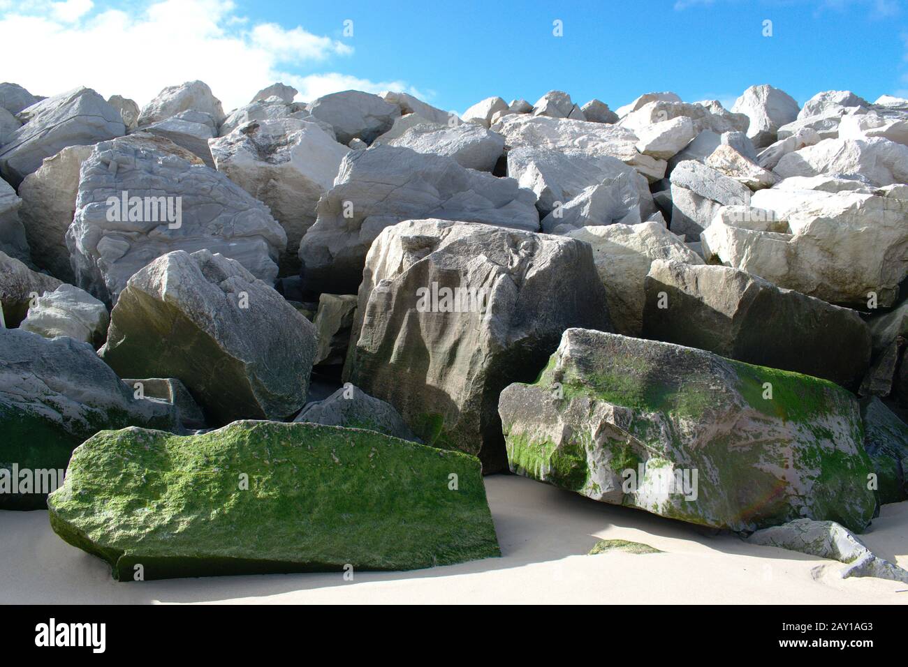 Sea Breaker realizzato con roccia naturale con alghe che crescono su alcuni di loro e un cielo blu e alcune nuvole puffy Foto Stock