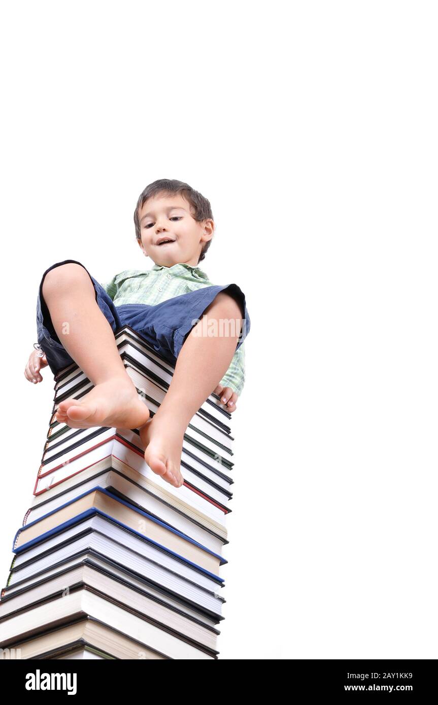 Carino ragazzo seduto su un mucchio grande di libri Foto Stock