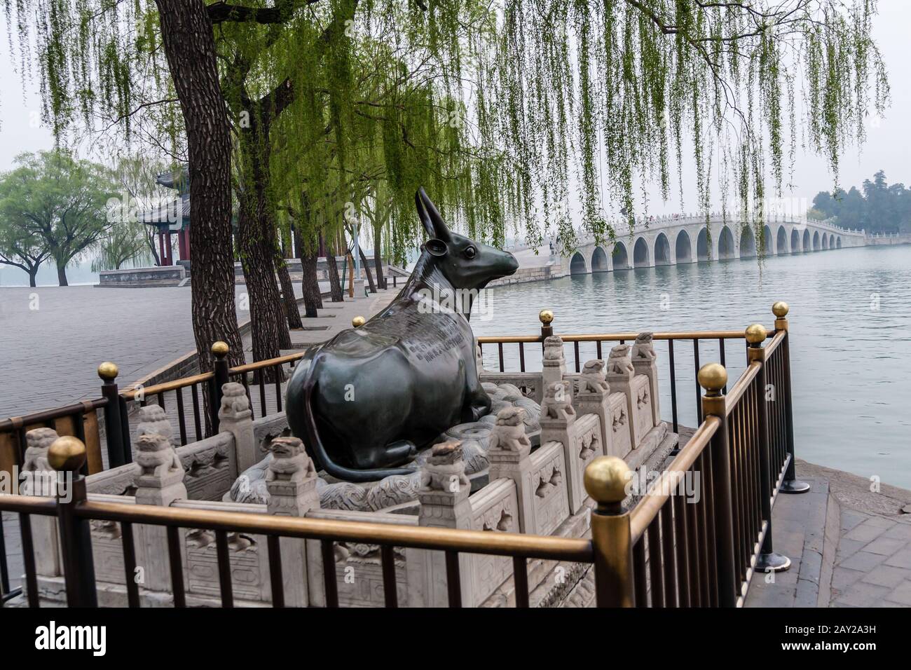 Una scultura di bue di bronzo sulla riva del Lago di Kunming e il Ponte dell'Arco della Seventeen del complesso del Palazzo d'Estate, Pechino Foto Stock