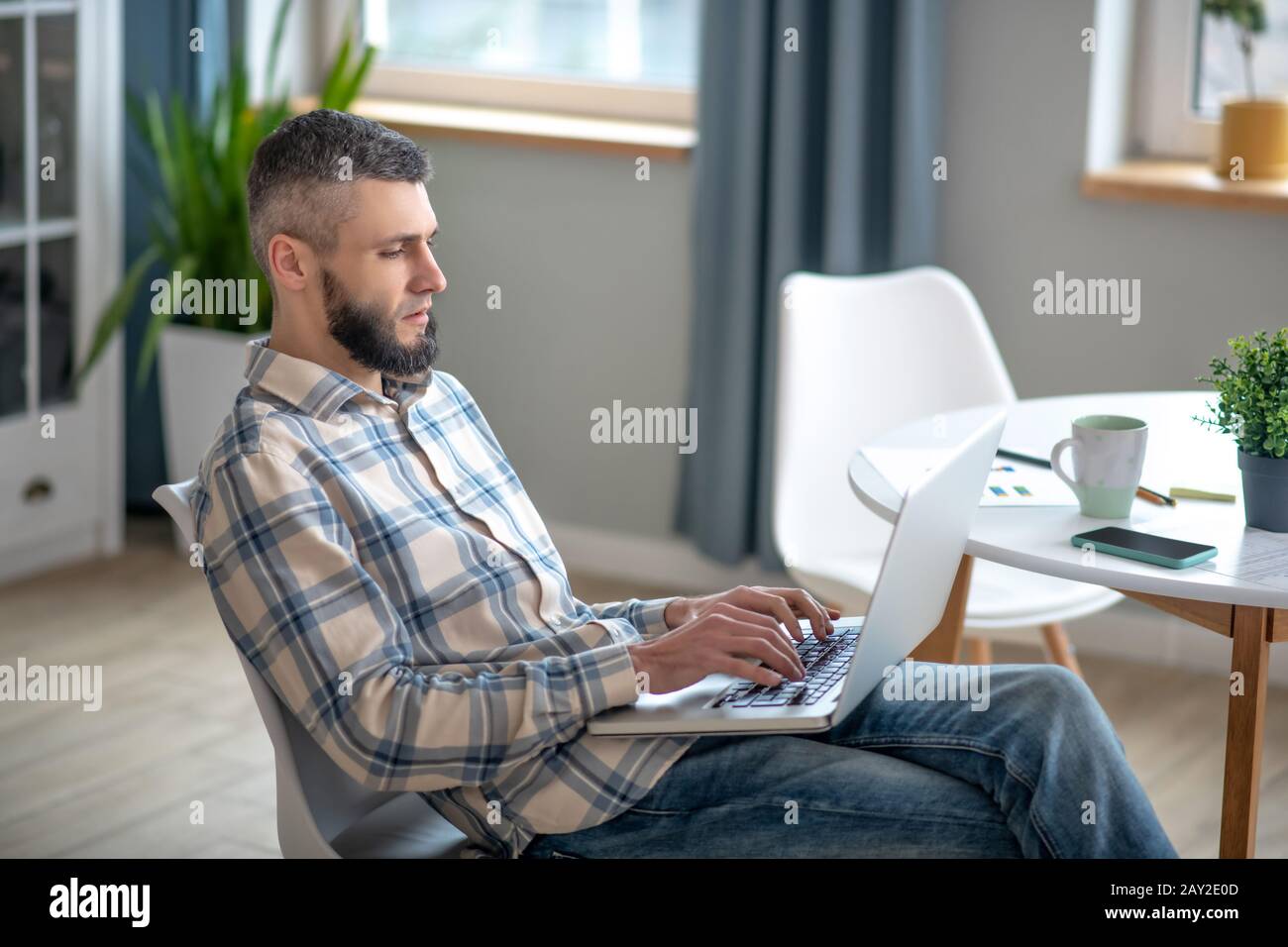 Giovane uomo seduto su una sedia che tiene il portatile nelle sue braccia. Foto Stock