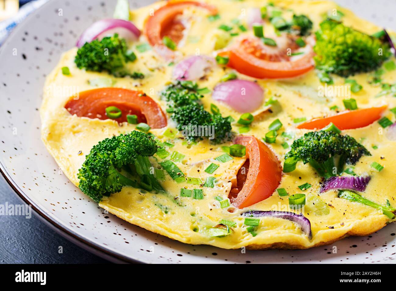 Frittata con broccoli, pomodori e cipolle rosse sul tavolo scuro. Frittata italiana con verdure. Foto Stock