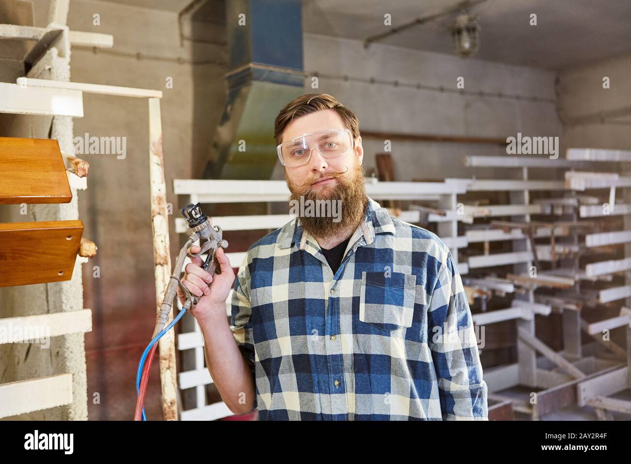 Pittore sicuro di sé con pistola a spruzzo nel negozio di vernice o nella macchina armadio Foto Stock