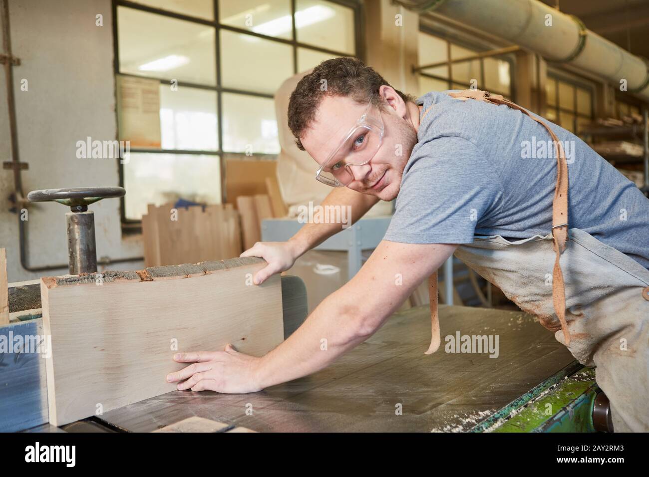 Apprendista falegname con occhiali di sicurezza durante la piallatura del legno sulla piallatrice Foto Stock