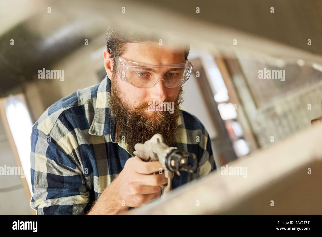 Falegname come pittore che usa la pistola di vernice mentre dipinge il legno nel negozio di vernice Foto Stock