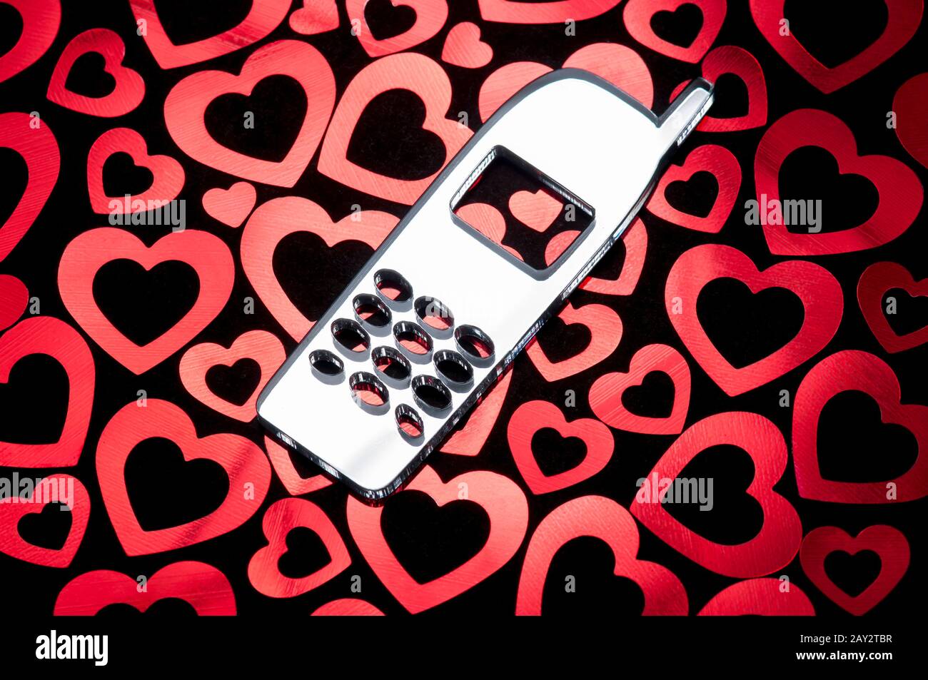 Cellulare vecchio stile appoggiato su un letto di romantico cuore rosso pronto per il messaggio di San Valentino Foto Stock