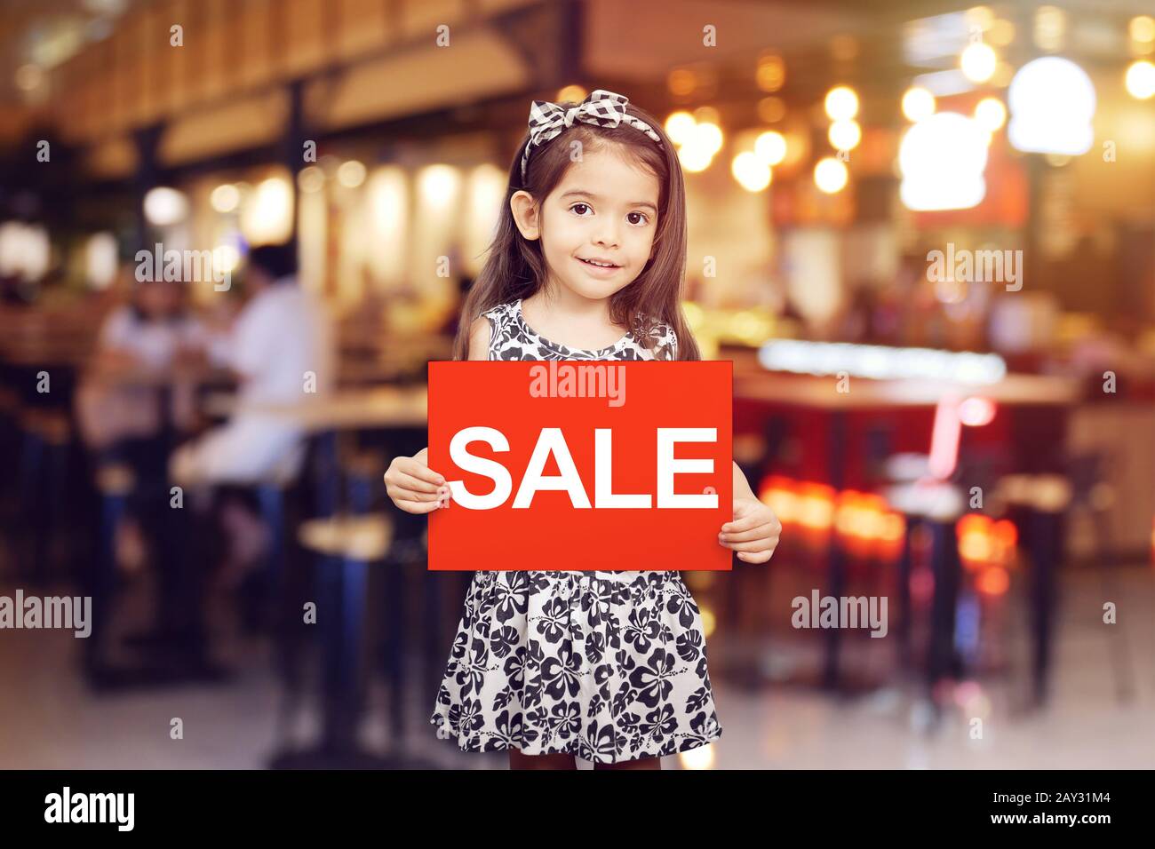 vendita sconto promozione per negozio concetto : adorabile ragazza tenuta segno rosso con vendita di testo in colore bianco di fronte al negozio, ristorante o caffè Foto Stock