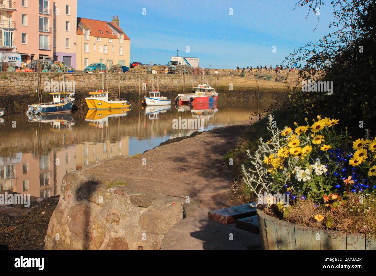 Vista vivace degli studenti di St Andrews seduti sul molo accanto al porto e in una giornata di sole dopo rasin con fiori colorati e barche da pesca Foto Stock