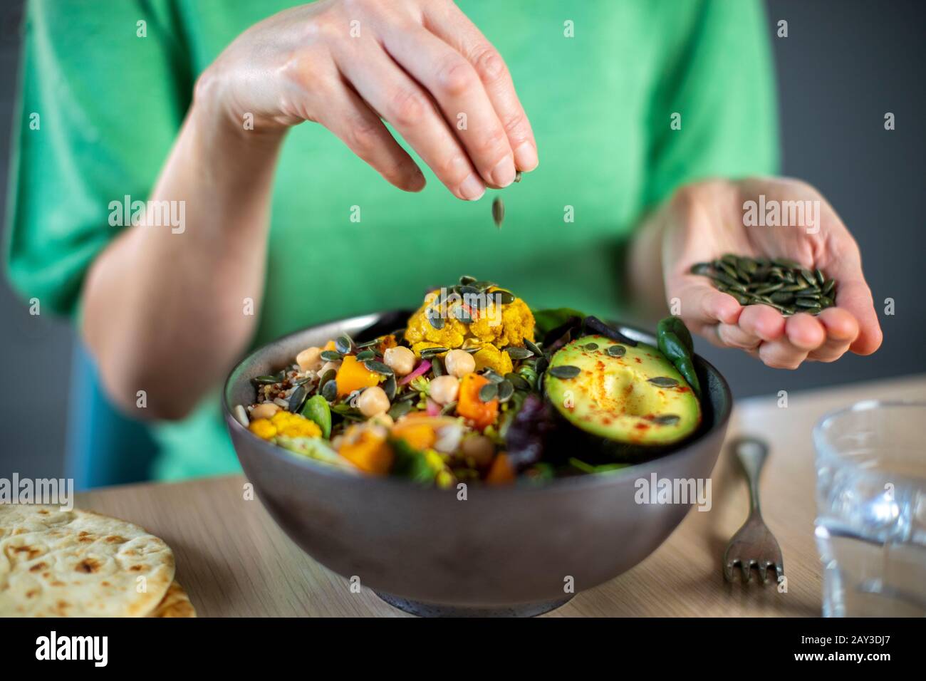 Close Up Of Woman Aggiungere Semi Di Zucca Al Pasto Sano Vegan In Bowl Foto Stock