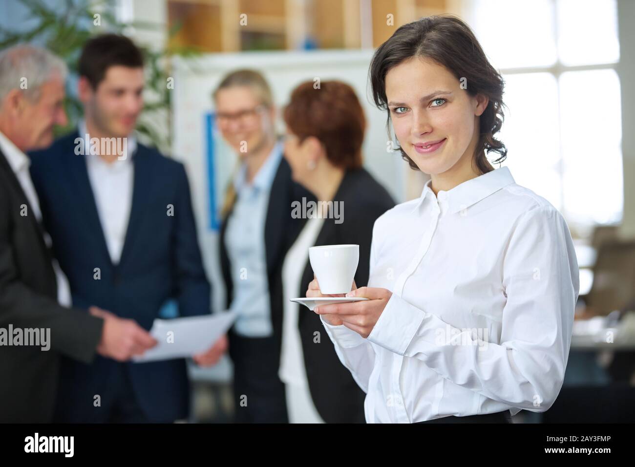 Donna sorridente che beve una tazza di caffè in ufficio Foto Stock