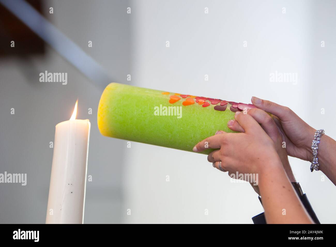 Primo piano delle mani della sposa e dello sposo che illuminano la loro candela verde di nozze insieme in un giorno di nozze, un evento emotivo nella cerimonia. Foto Stock