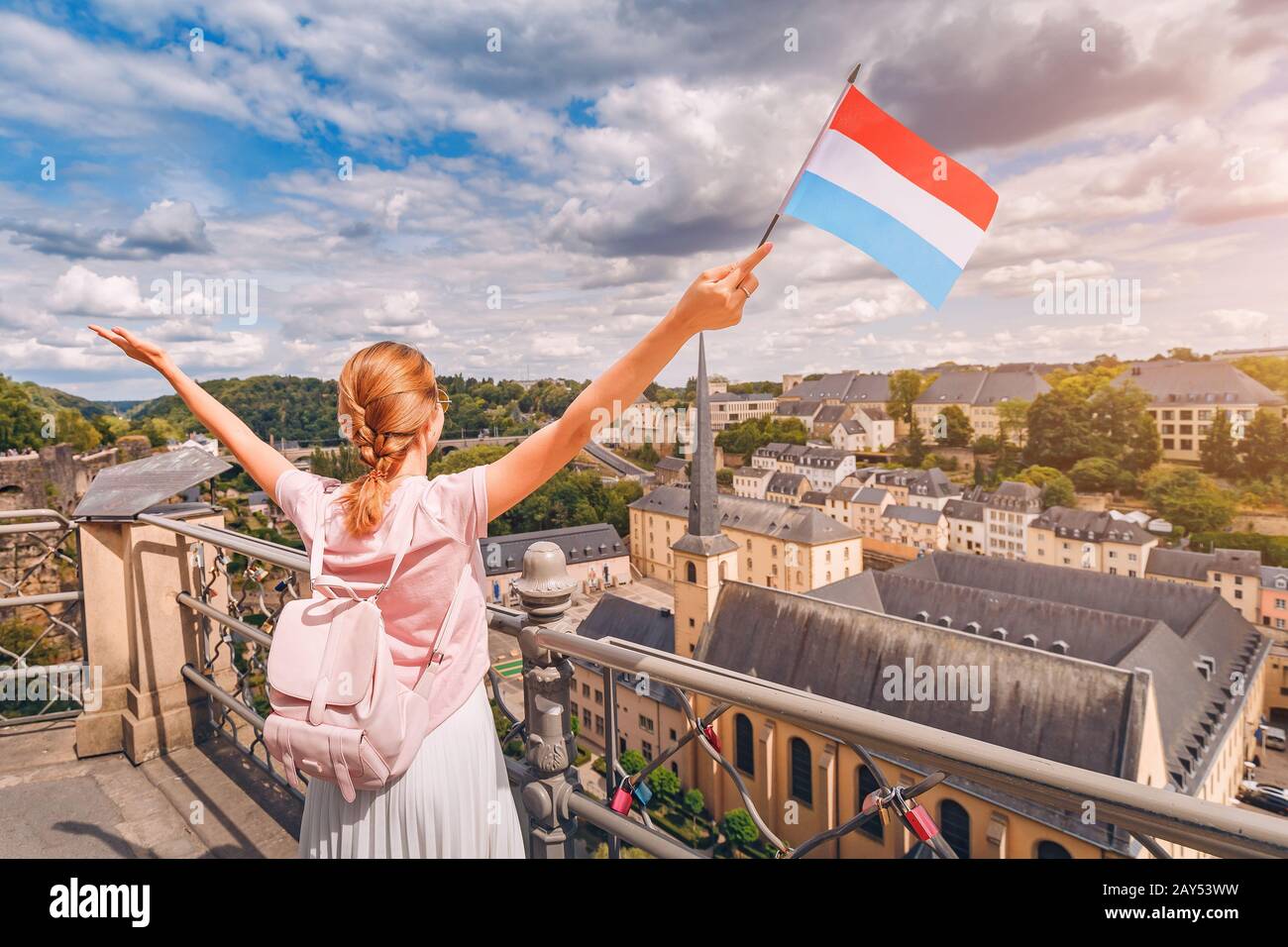 Una ragazza felice del viaggiatore tiene la bandiera del Lussemburgo e ammira la zona di Grund dalla piattaforma di osservazione. Turismo, ricreazione e vita nel paese. Foto Stock