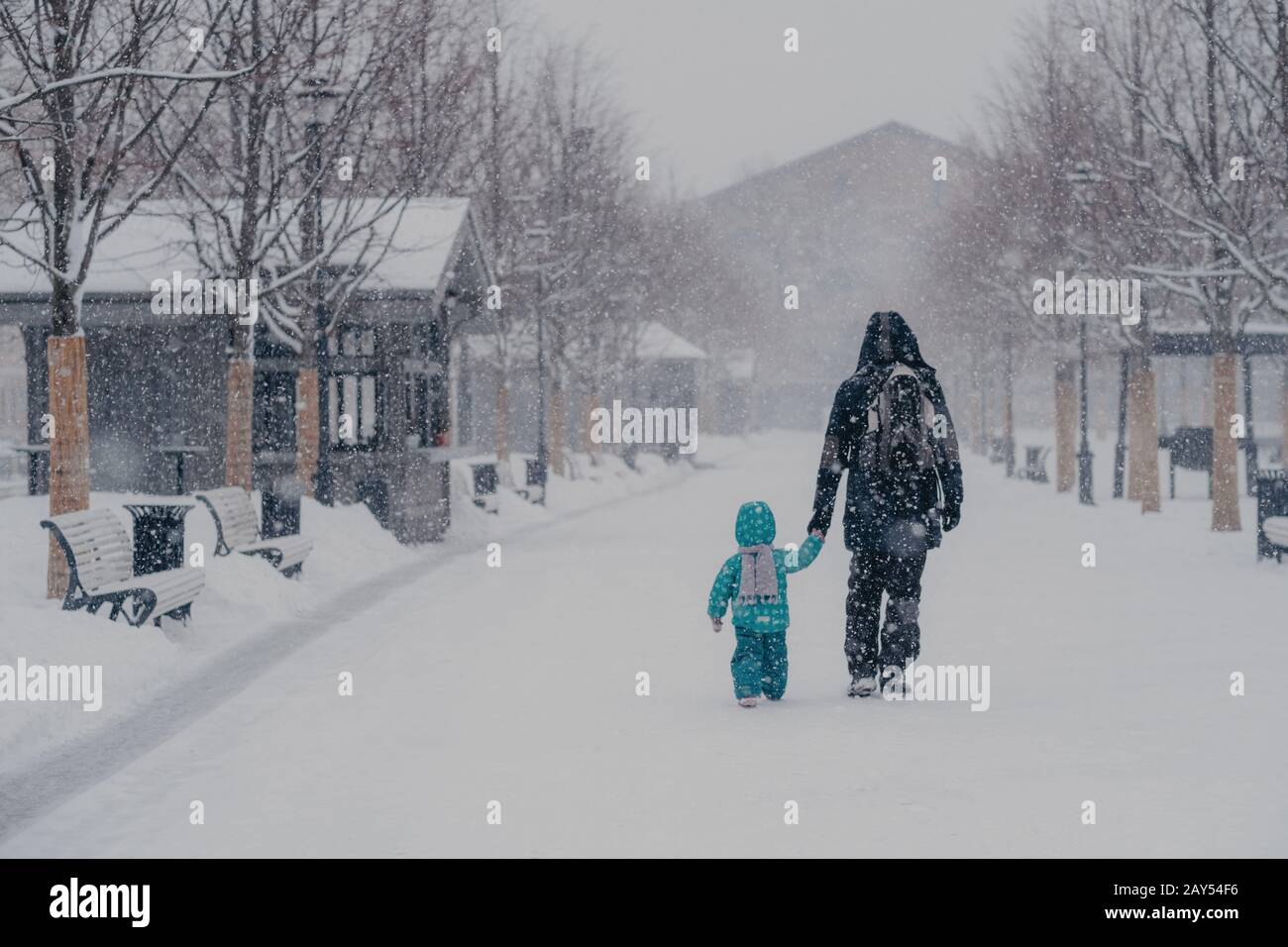 Tiro all'aperto di piccolo bambino e padre coprire la distanza, essere sul modo di casa, tenere le mani, godersi inverno nevoso tempo. Vista posteriore della gente che cammina su st Foto Stock