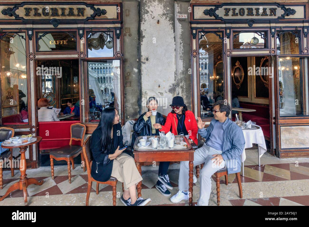 Una famiglia asiatica si siede a un tavolo e gode di una tazza di caffè presso la famosa caffetteria Florian in Piazza San Marco. Venezia. Italia Foto Stock