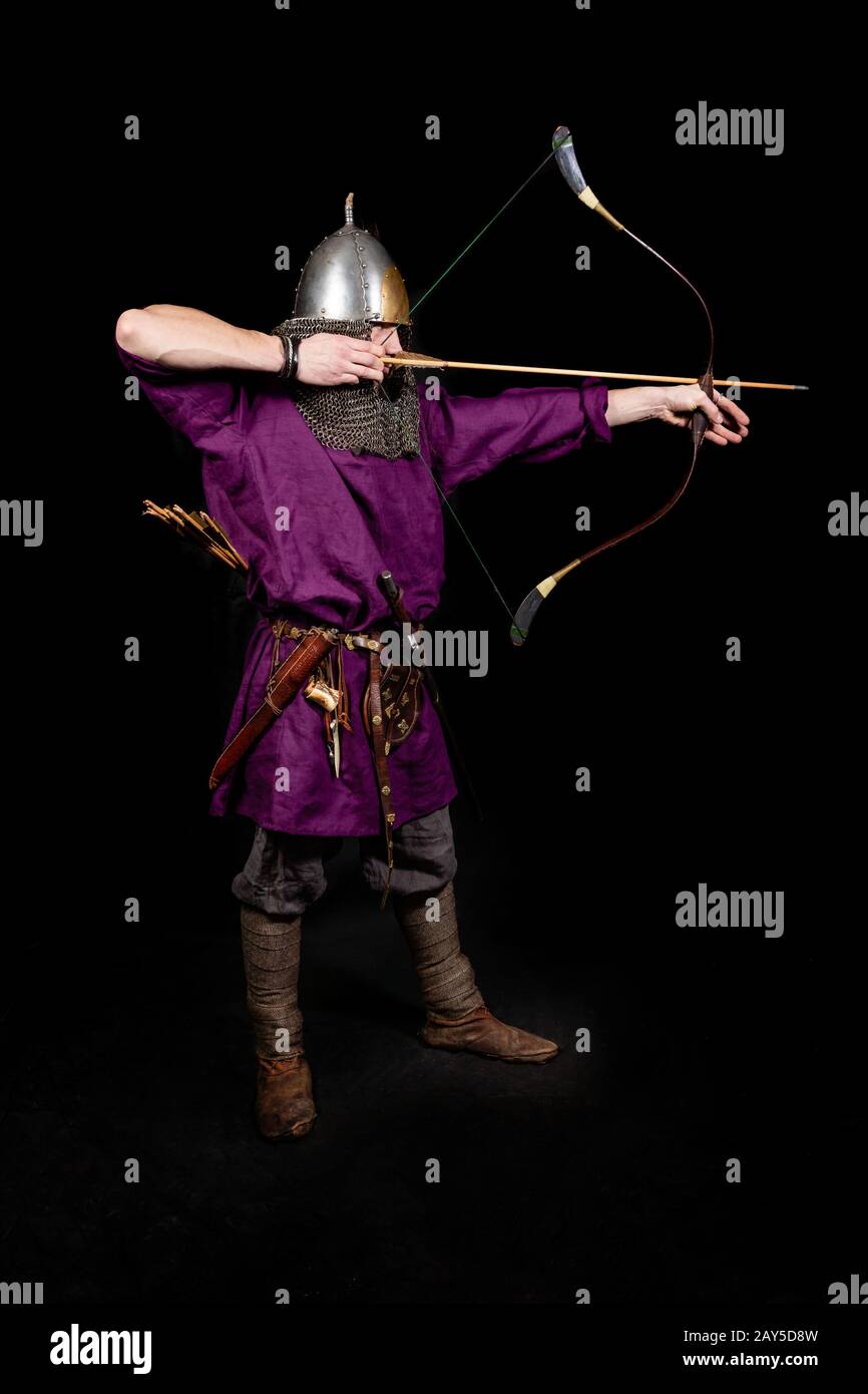 l'uomo in abito medievale, camicia viola e casco tiene un arco. l'ironia: il cupido abbastanza maturo Foto Stock