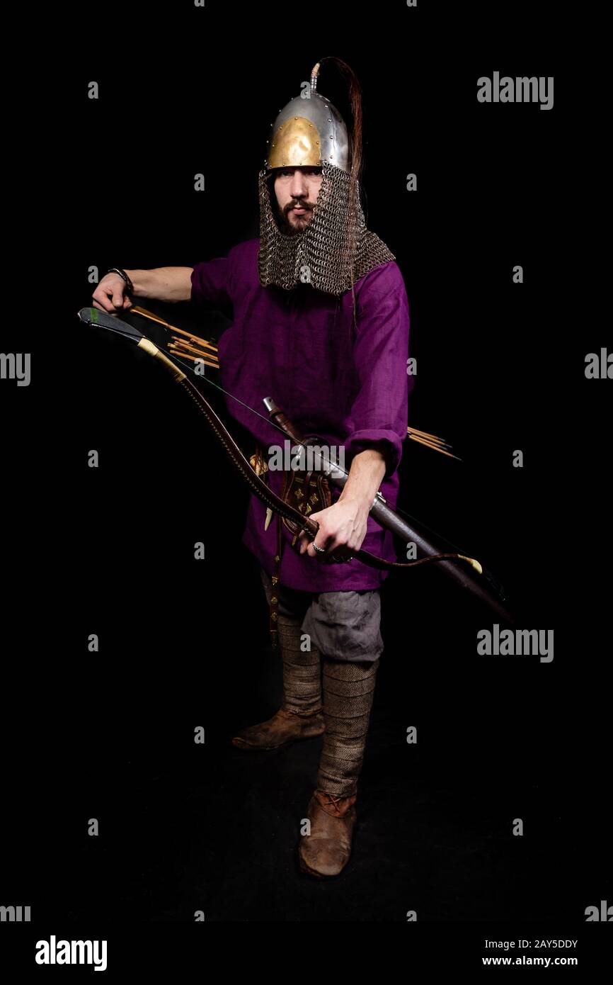 l'uomo in abito medievale, camicia viola e casco tiene un arco. l'ironia: il cupido abbastanza maturo Foto Stock