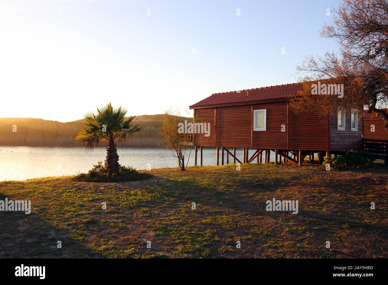 casa rossa su un lago con palme e tramonto Foto Stock