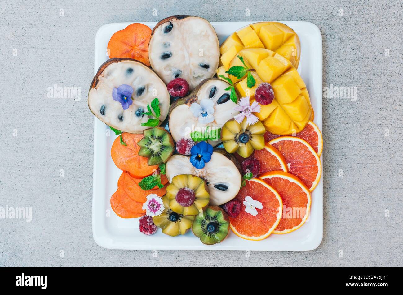 Piatto di frutta tropicale esotica. Kiwi d'oro, persimone, lampone, mango, arance e menta. Piatto di frutta matura decorata fresca. Concep. Cibo Foto Stock