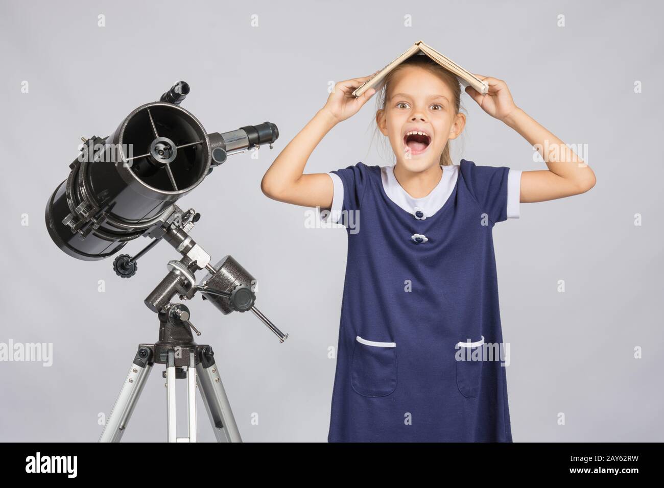 Schoolgirl copriva la testa con un libro di testo e di piangere guardando il telaio, stando in piedi presso il telescopio Foto Stock