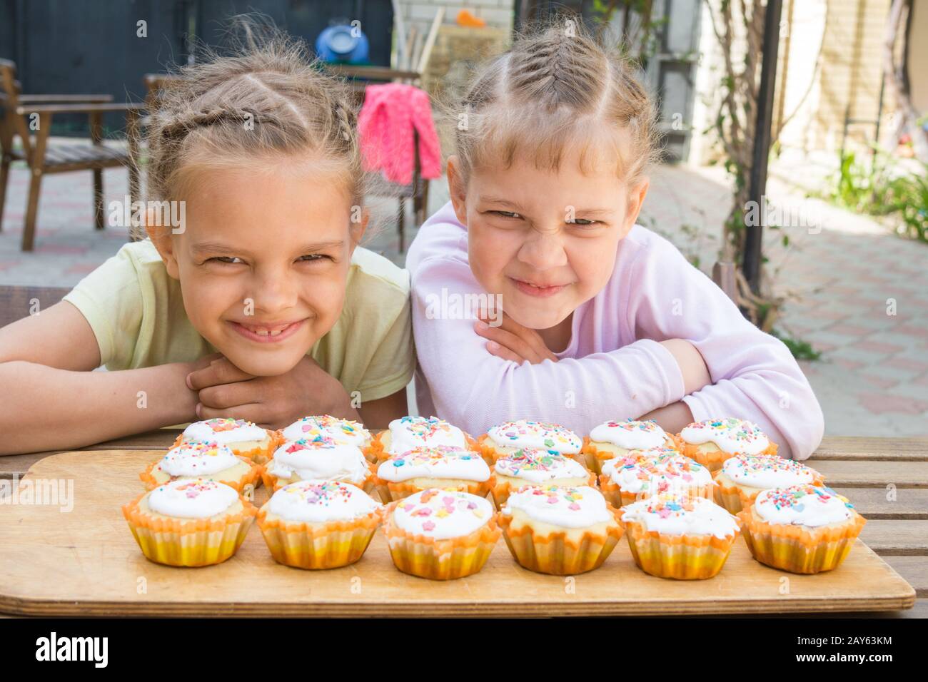 Due ragazze fingendo facce buffe, seduti di fronte tortine di pasqua Foto Stock