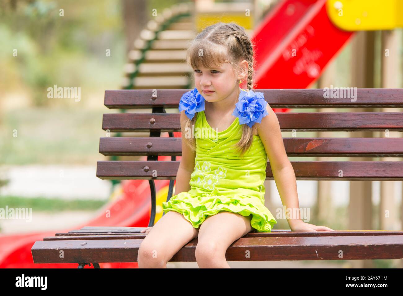 Ritratto di sconvolgere bambina di cinque anni che è seduto sul banco di lavoro sullo sfondo del parco giochi Foto Stock