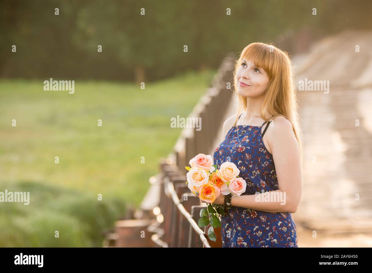 Ragazza giovane con un mazzo di rose in piedi sul ponte sullo sfondo sfocato fogliame Foto Stock