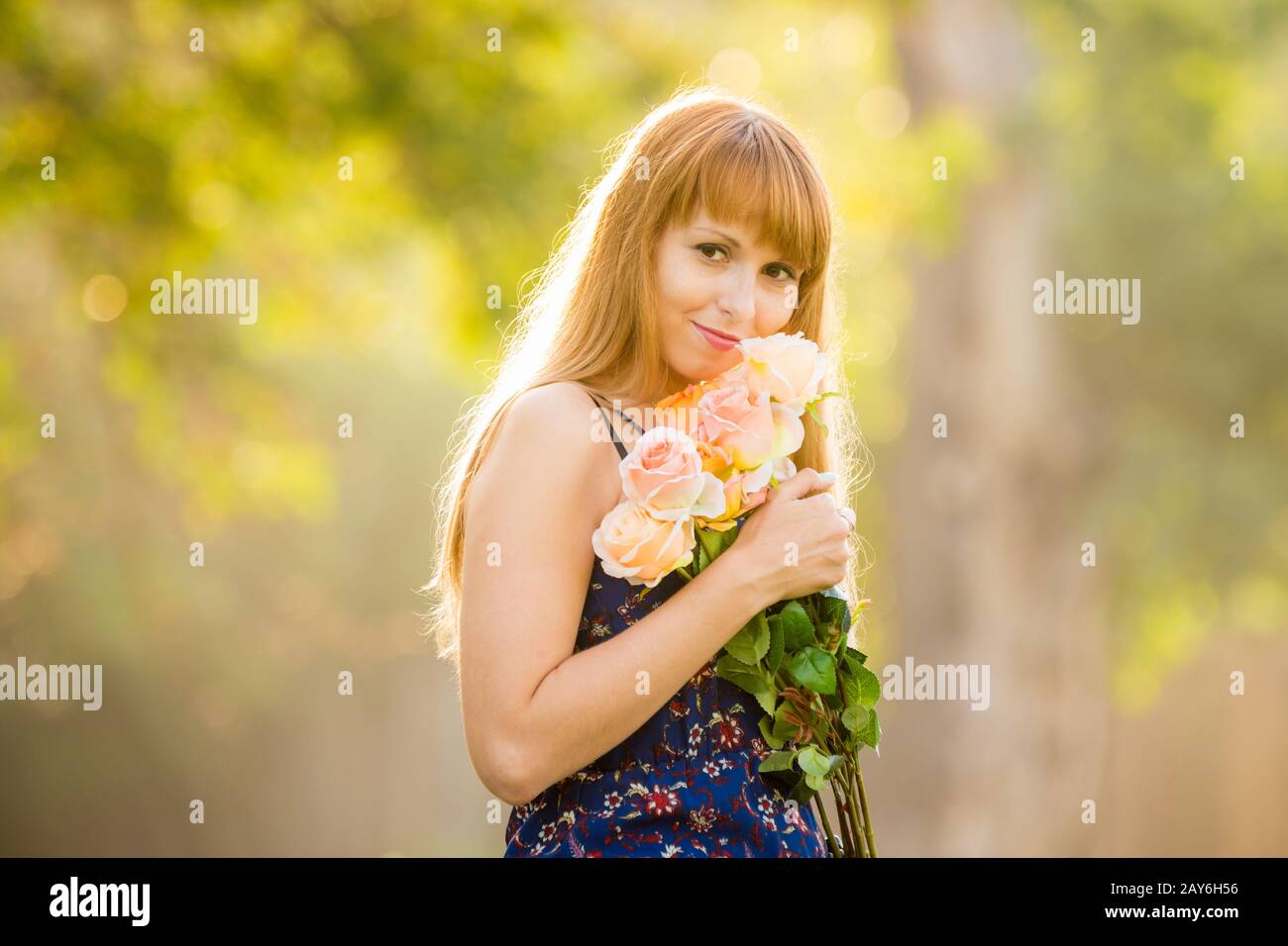 Giovane e bella ragazza sexy in piedi con un mazzo di rose su uno sfondo di colore verde soleggiata sfocato Foto Stock