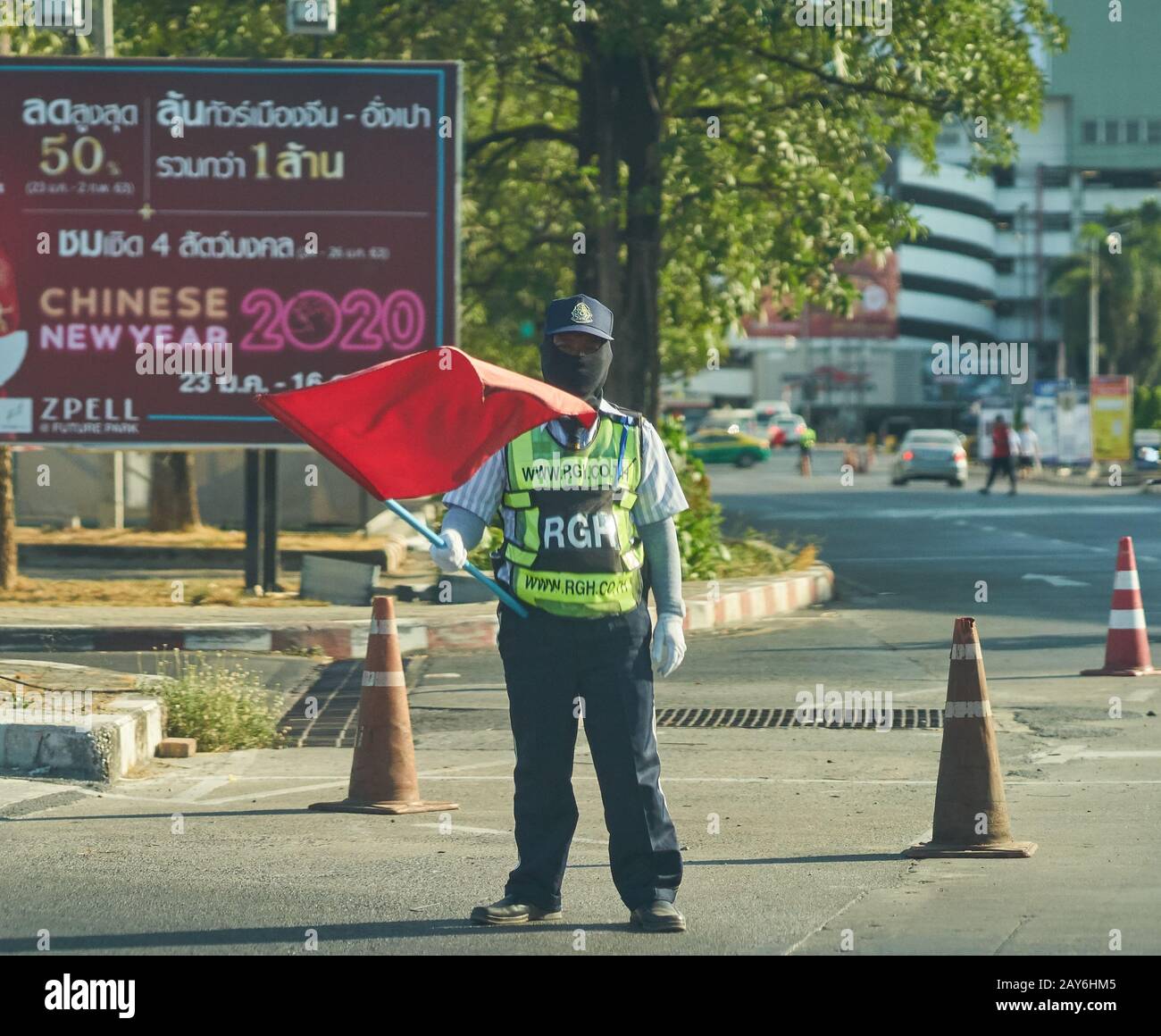 Una guardia di sicurezza con una bandiera rossa, che indossa una maschera facciale, di fronte a un tabellone per il Capodanno cinese. Foto Stock