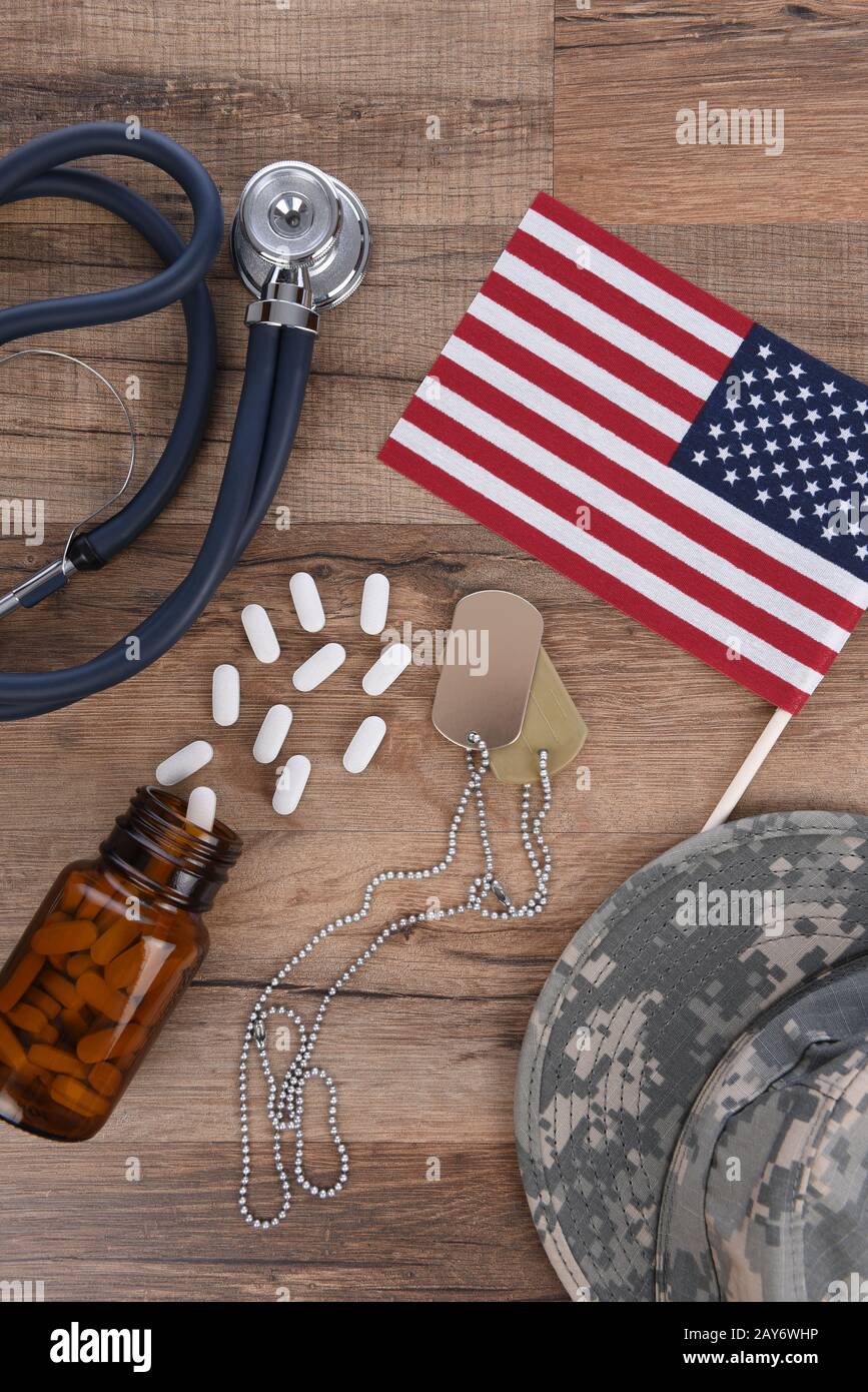 Concetto Di Assistenza Sanitaria Militare. Tag cane, stetoscopio, pillole, cappello camouflage e bandiera americana su uno sfondo di legno. Foto Stock