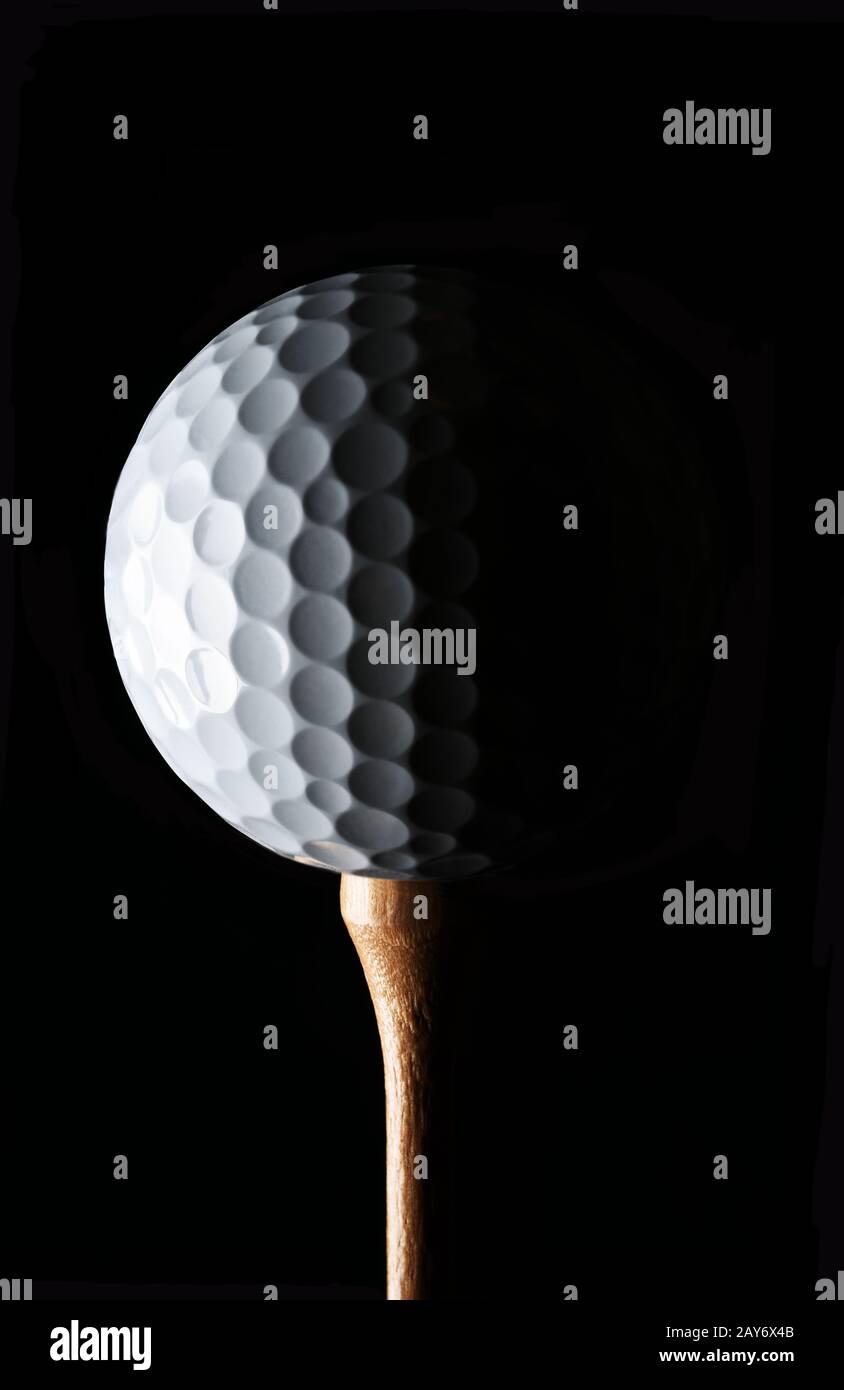 Golf Still Life. Closeup bassa palla da golf chiave su tee di legno con forte luce laterale, contro uno sfondo nero. Foto Stock