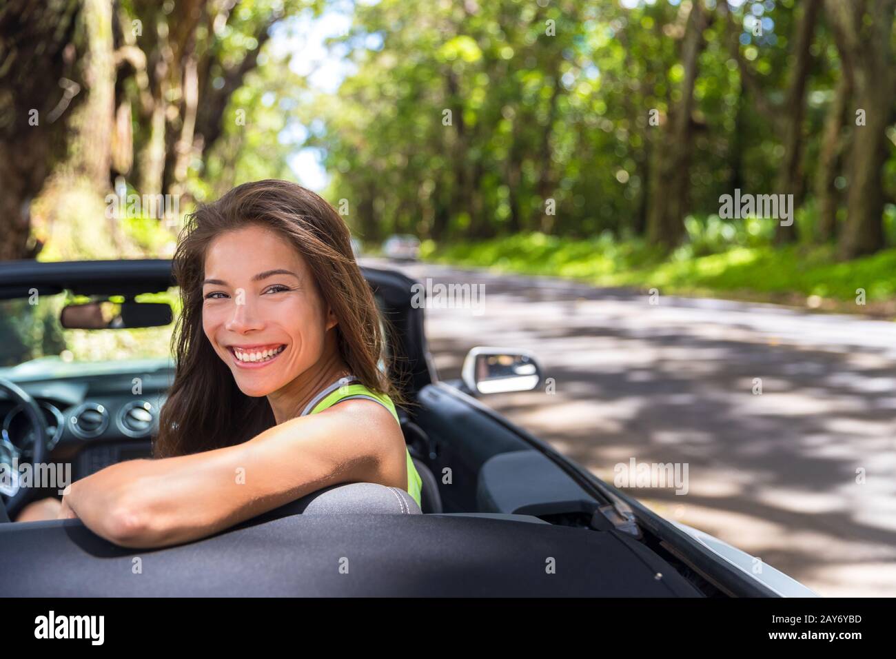 Felice giovane donna asiatica rilassante in auto convertibile in vacanza estiva viaggio su strada. Destinazione di viaggio in auto attraverso strade naturali. Foto Stock